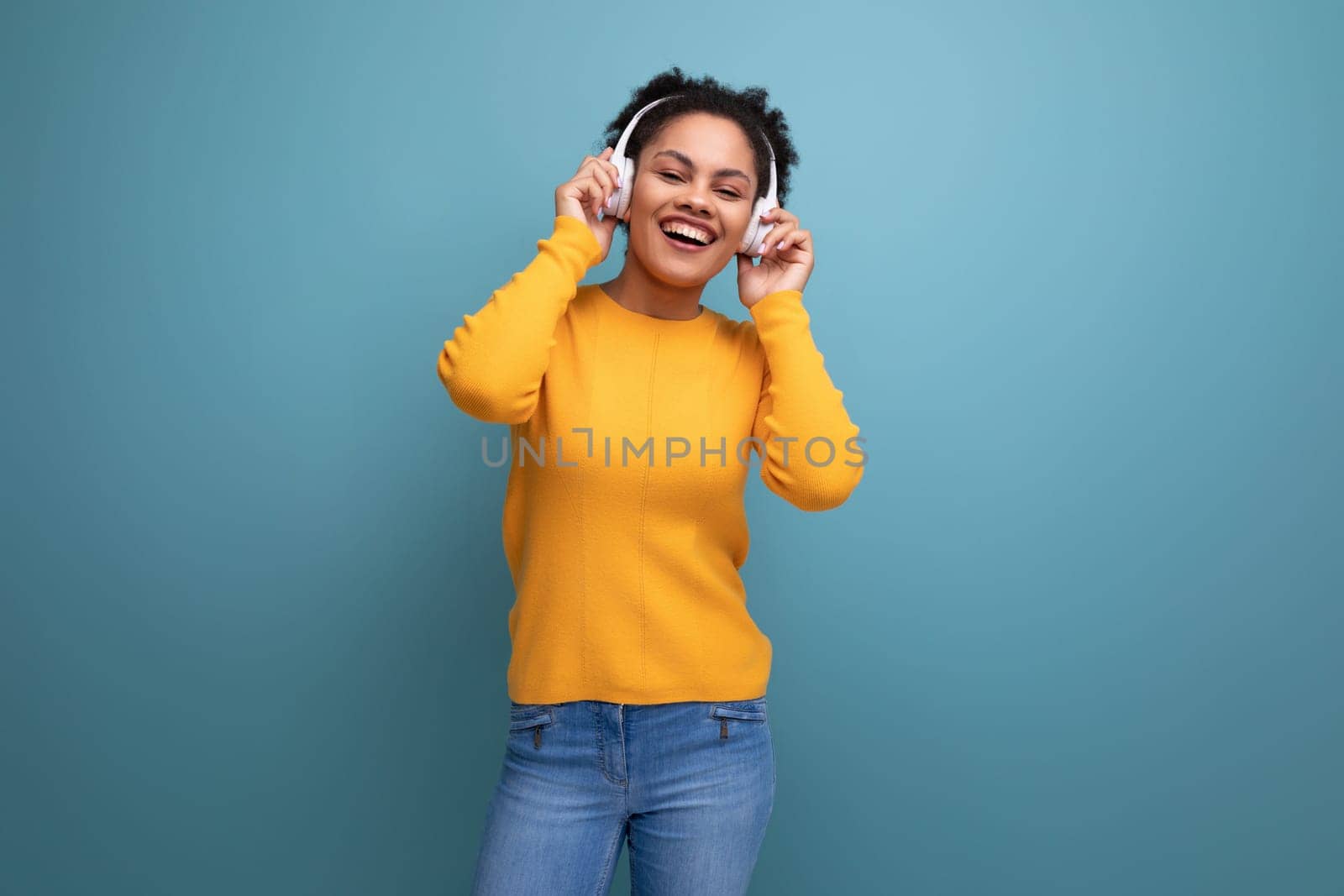 cheerful young hispanic business woman with black curly hair listening to music in white headphones.