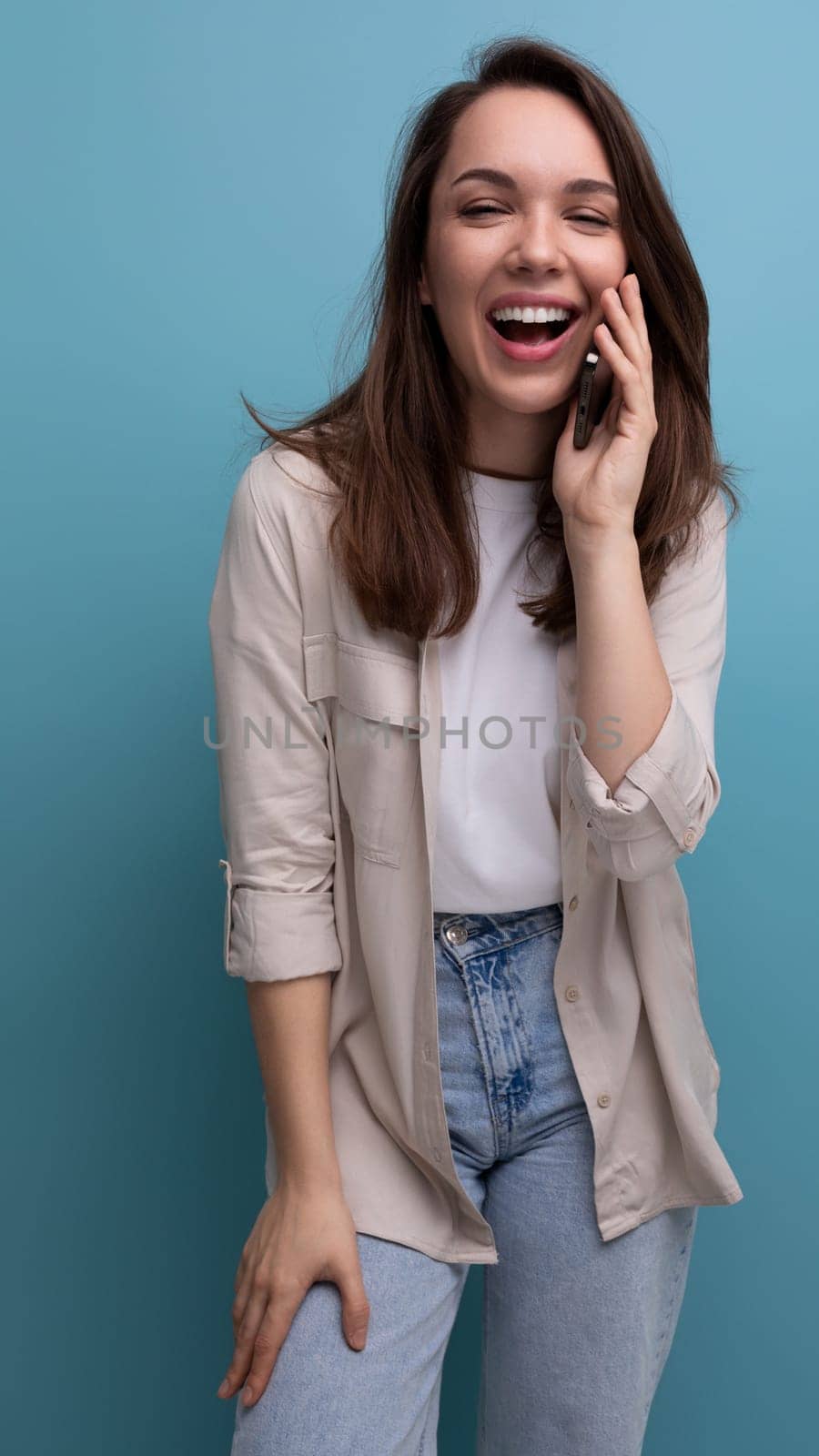 positive cheerful 30s brunette woman in shirt talking on the phone.