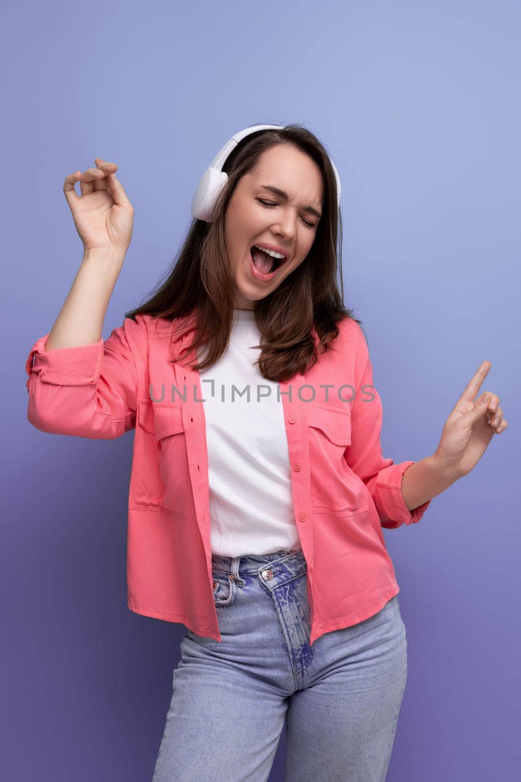enjoying brunette young woman with dark hair below her shoulders in a shirt and jeans with wireless headphones.
