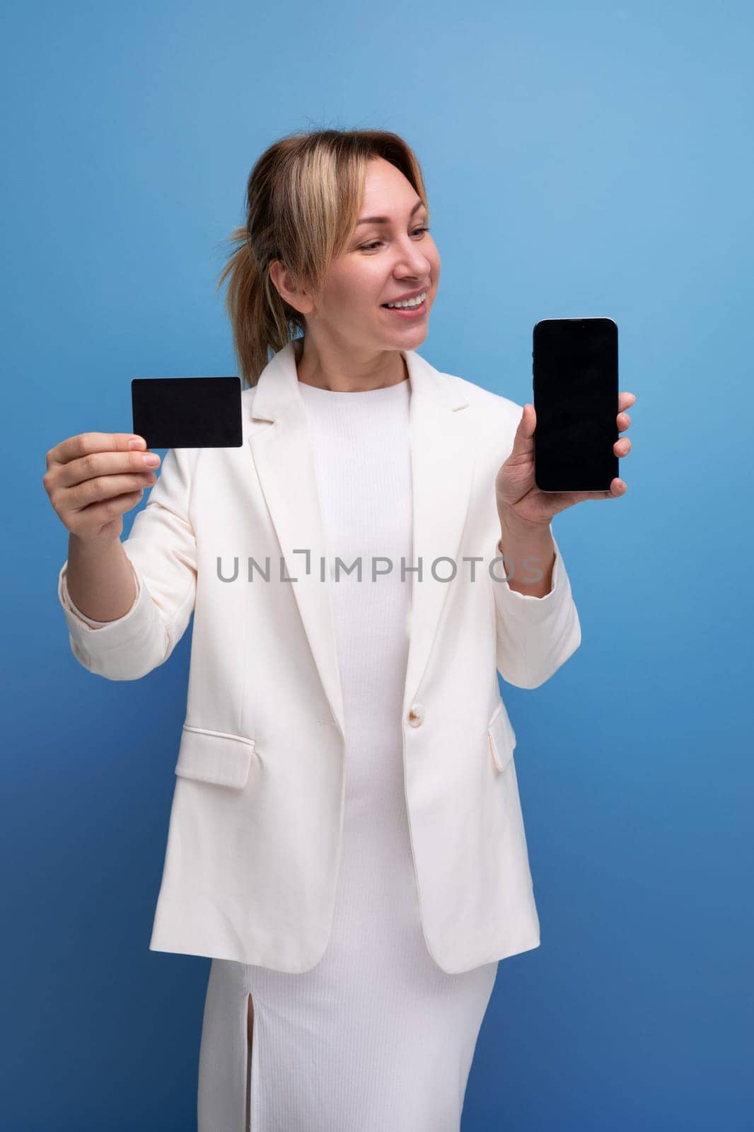 pretty young fair-haired business woman in a jacket and dress joyfully uses online payments with a bank card.