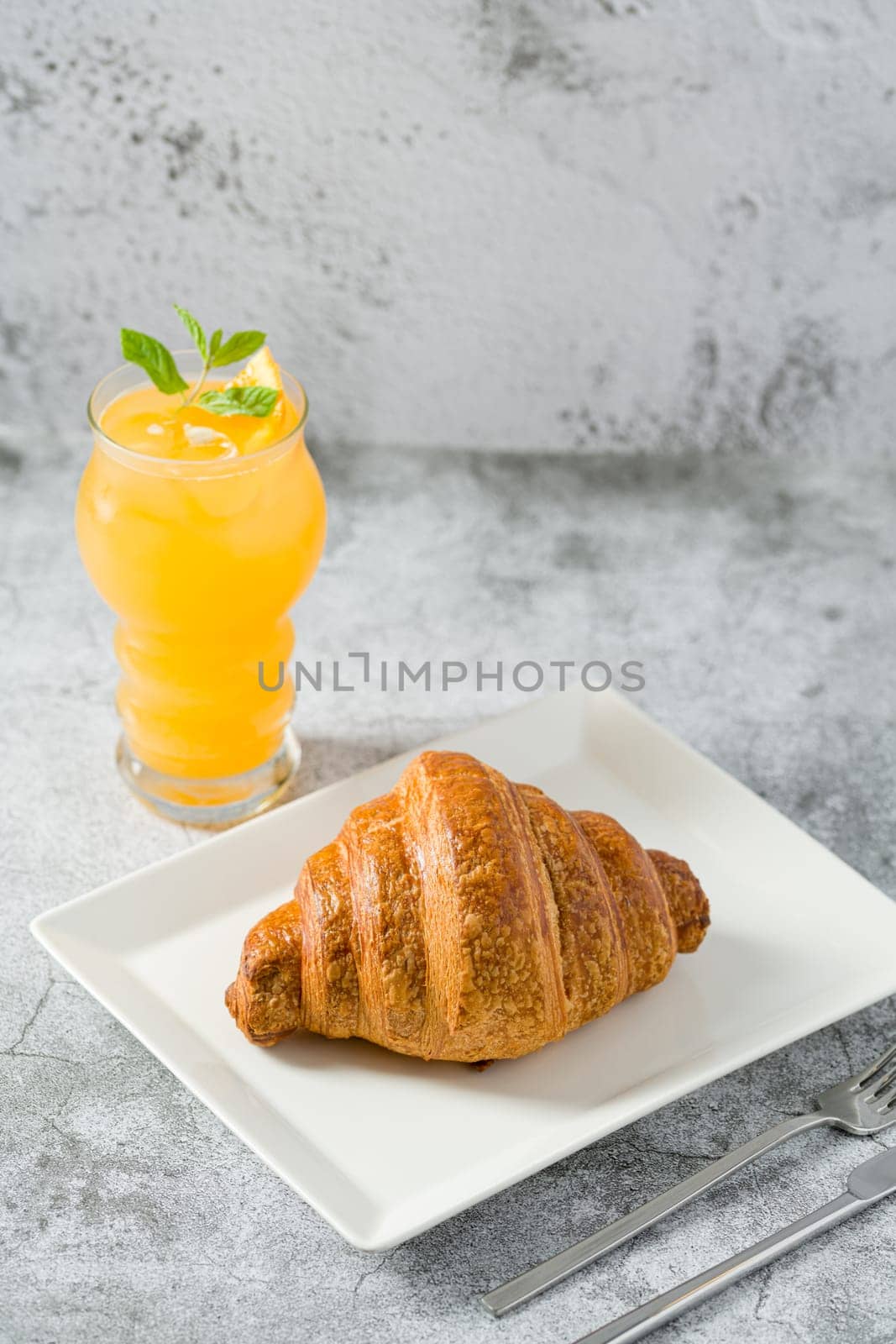 Croissant on white porcelain plate on light stone table