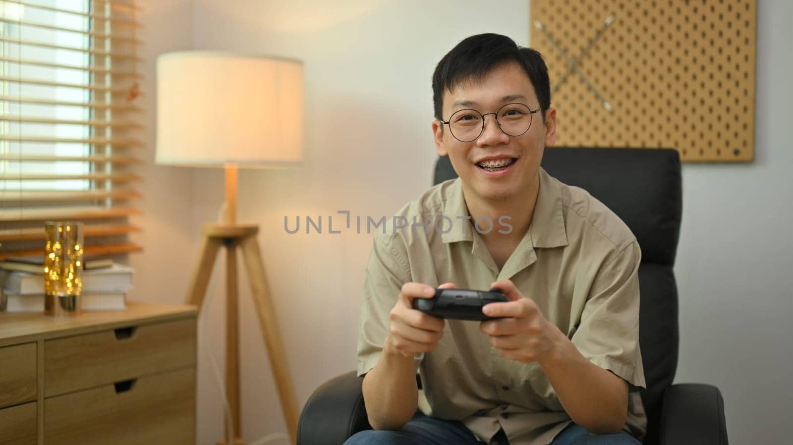 Man in casual clothes and glasses holding wireless controller playing video game. Entertainment, technology and hobby concept by prathanchorruangsak