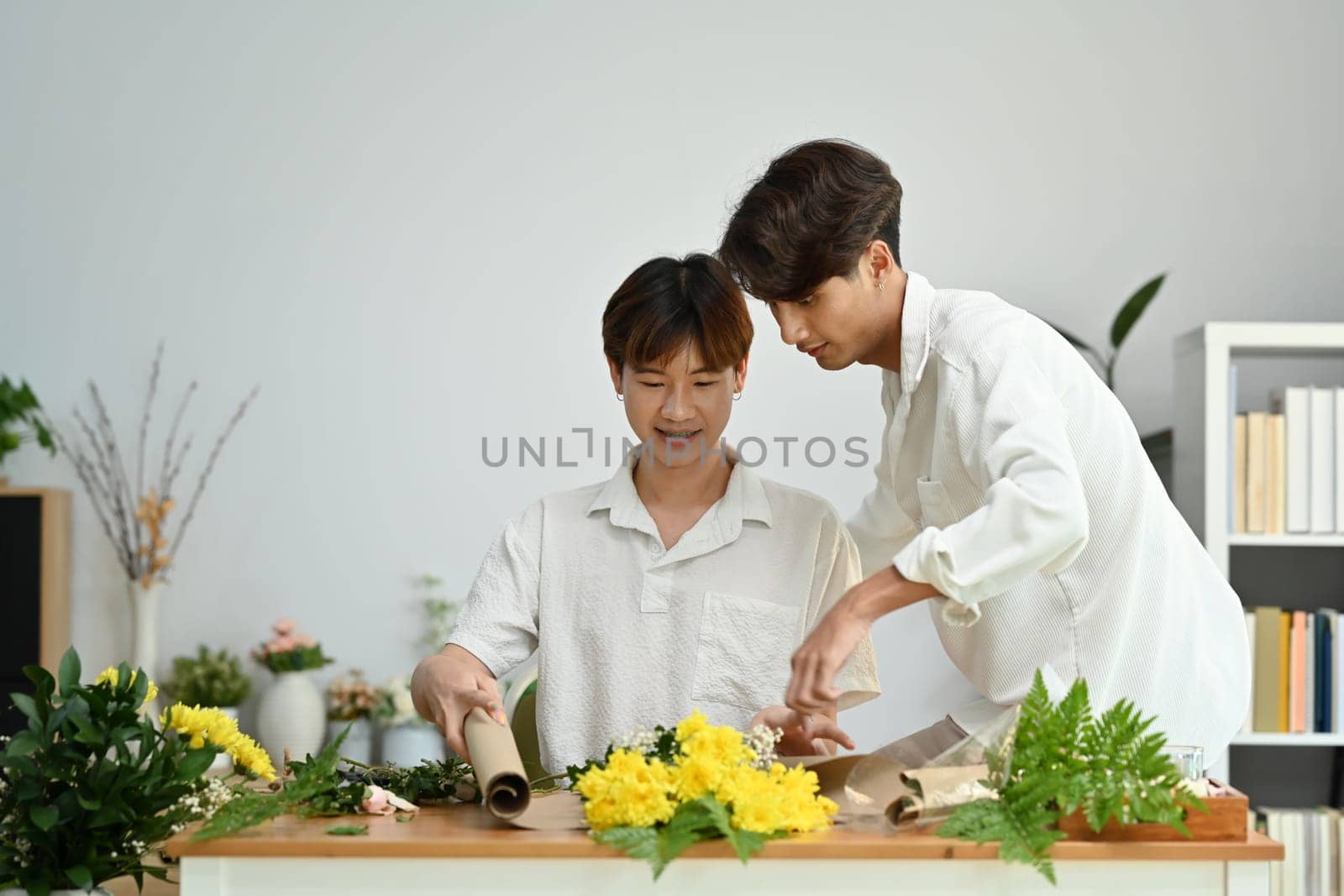 Cheerful gay couple arranging flowers, spending good time together at home. LGBT, love and lifestyle relationship concept by prathanchorruangsak