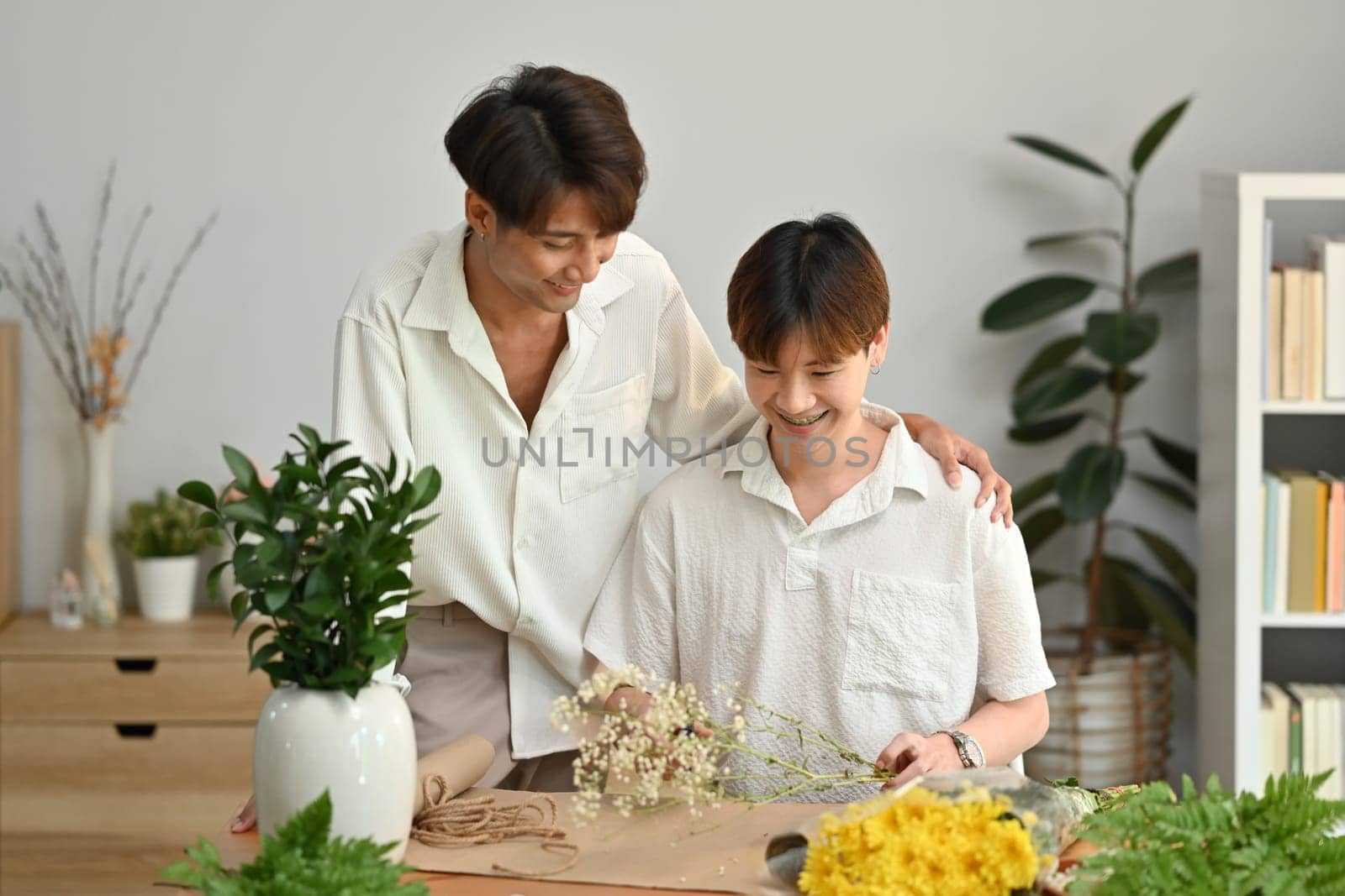 Cheerful gay couple arranging flowers, spending good time together at home. LGBT, love and lifestyle relationship concept by prathanchorruangsak