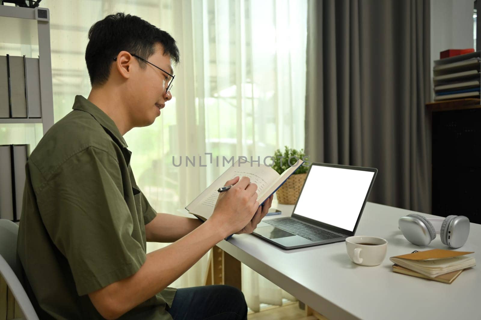 Male freelancer working remotely on laptop in living room, and making notes on notebook.