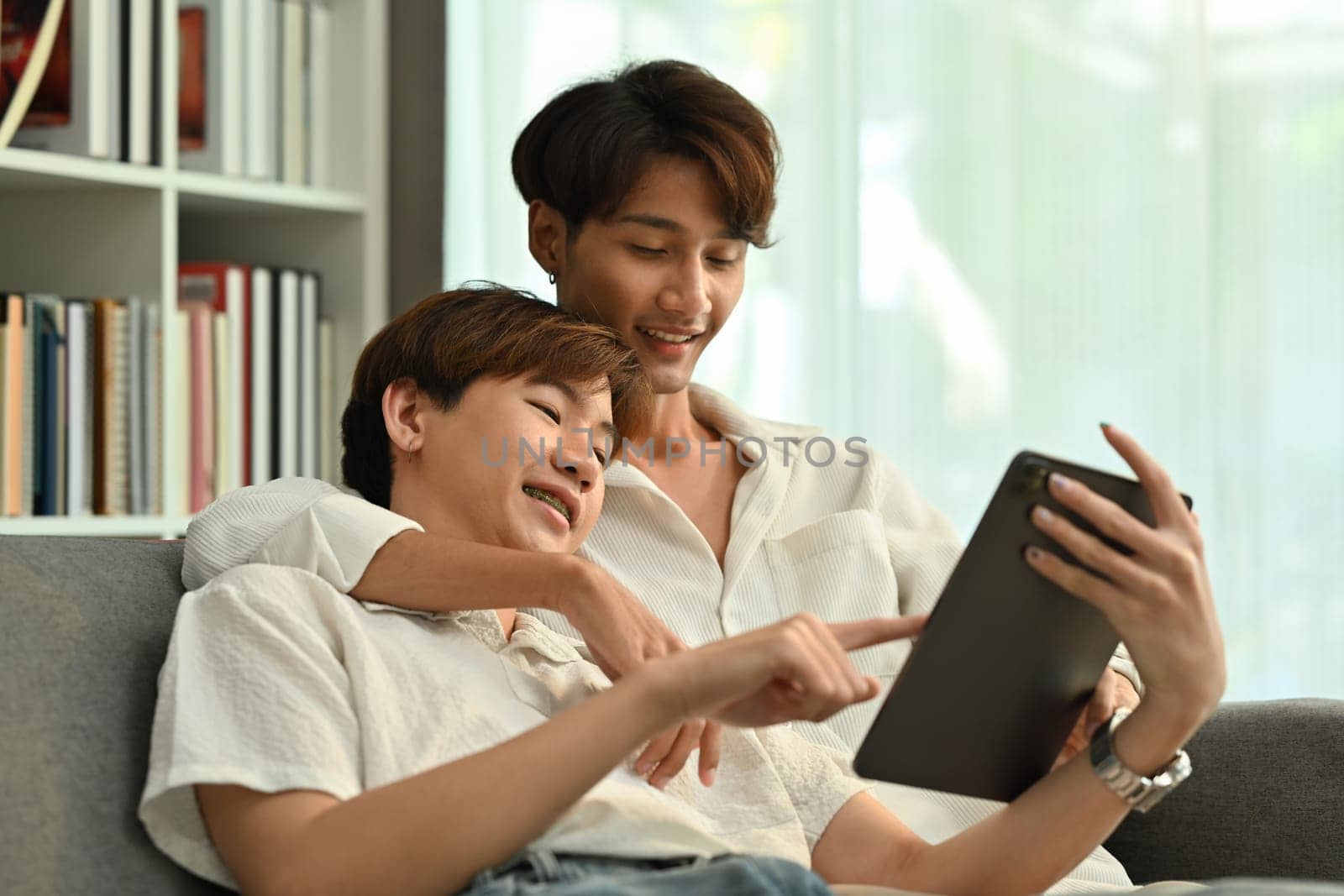 Passionate homosexual couple relaxing on couch and browsing internet on digital tablet. LGBT, love and lifestyle concept by prathanchorruangsak