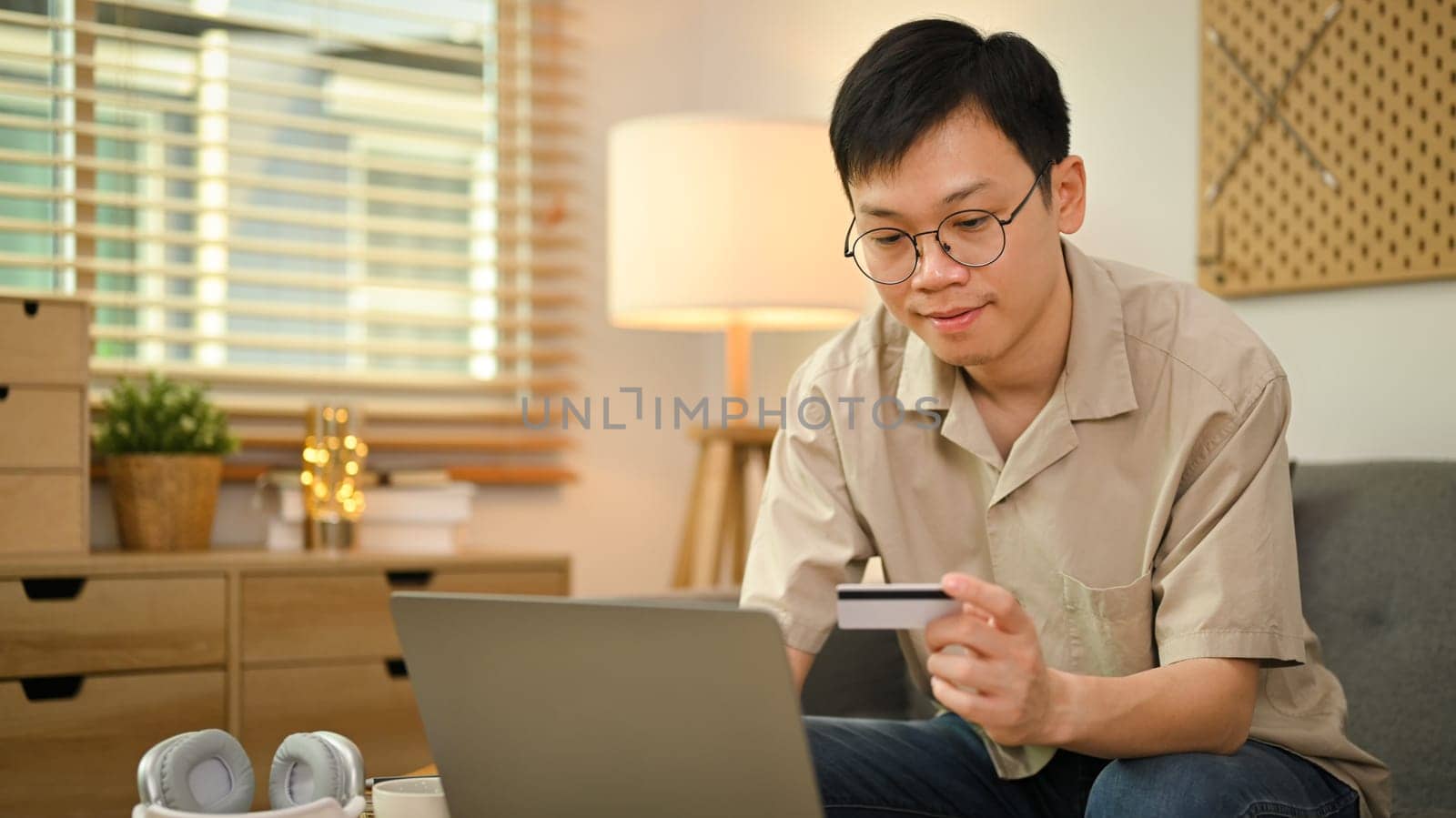 Millennial man in casual clothes holding credit card and using laptop for making orders via iInternet or online payment.