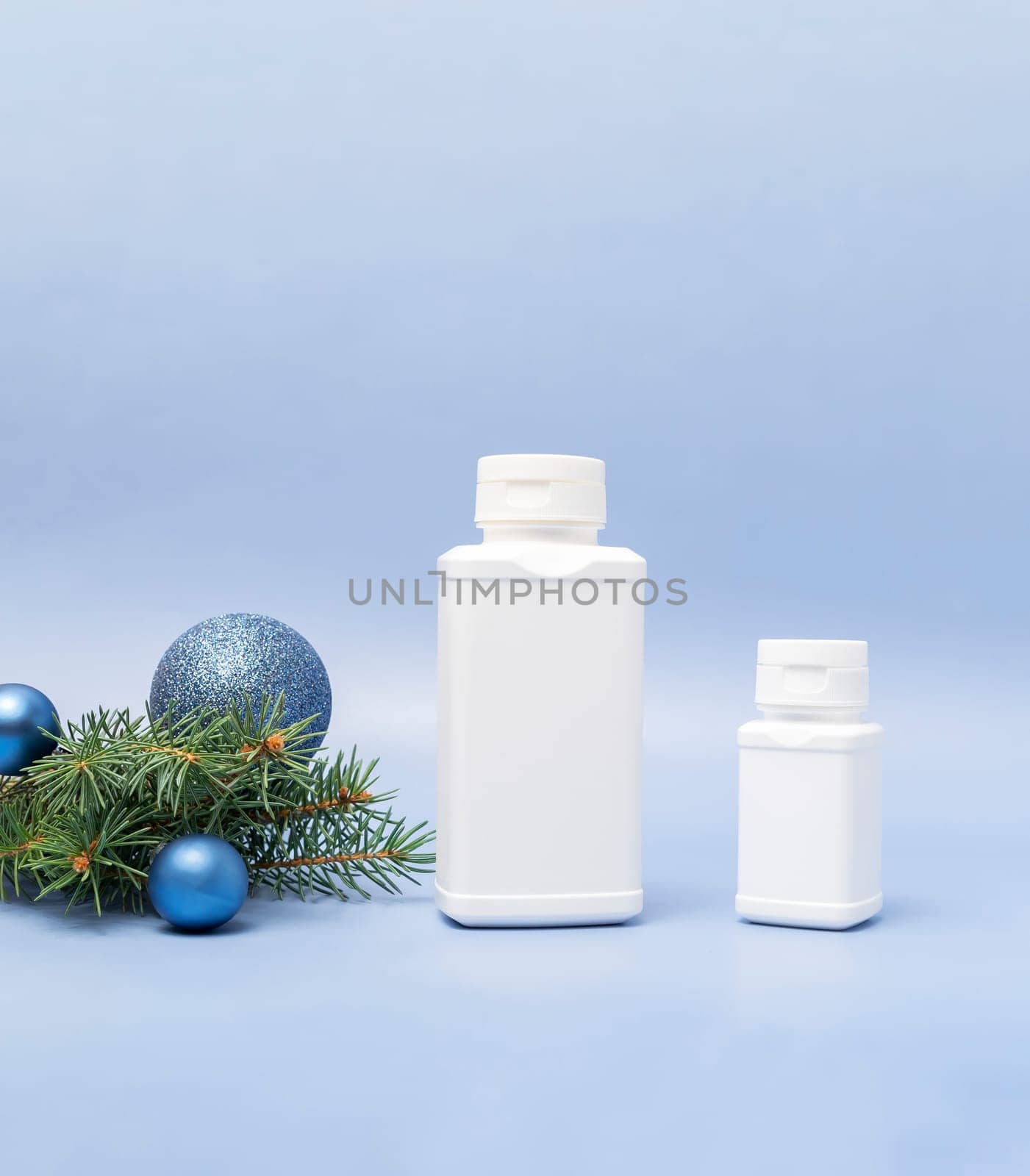 Merry Christmas pharmacy white bottles of pills, tablets, drugs, Christmas tree, sparkling toy balls on blue background. Winter holidays, New Year medical concept. Vertical plane