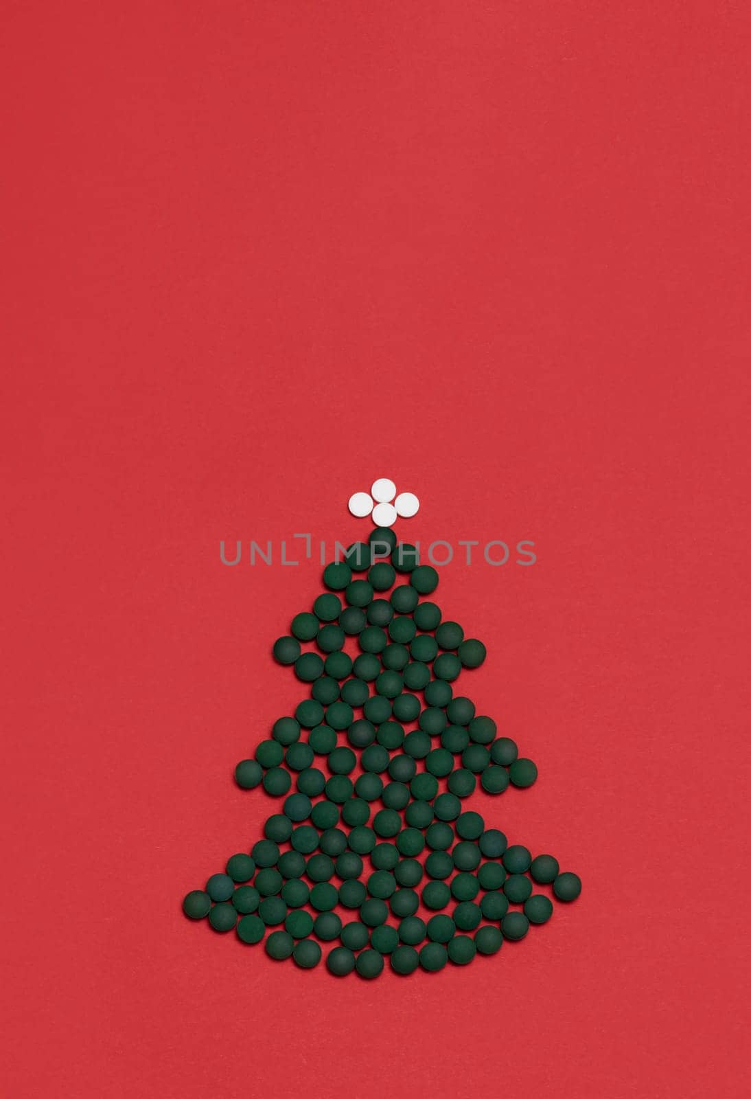 Red background, medicine mockup, Christmas tree made of green white pills,tablets,vitamins spirulina. Merry Christmas, Happy New Year concept, pharmacy postcard,flatly, top view, copy space Vertical