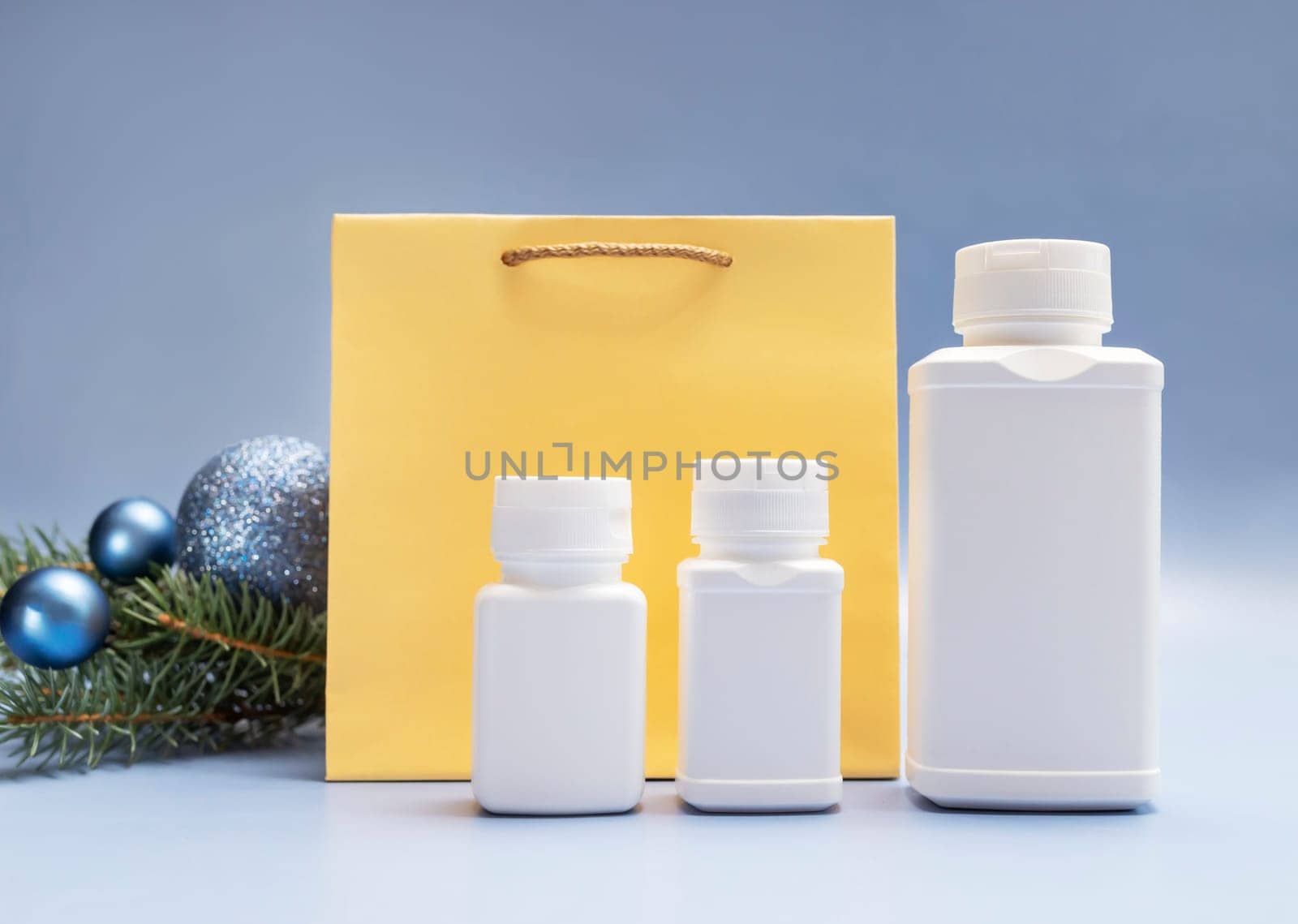 Christmas pharmacy white bottles of pills, golden paper package, Christmas tree, sparkling toy balls on blue background. Winter holidays, medical concept. Horizontal plane