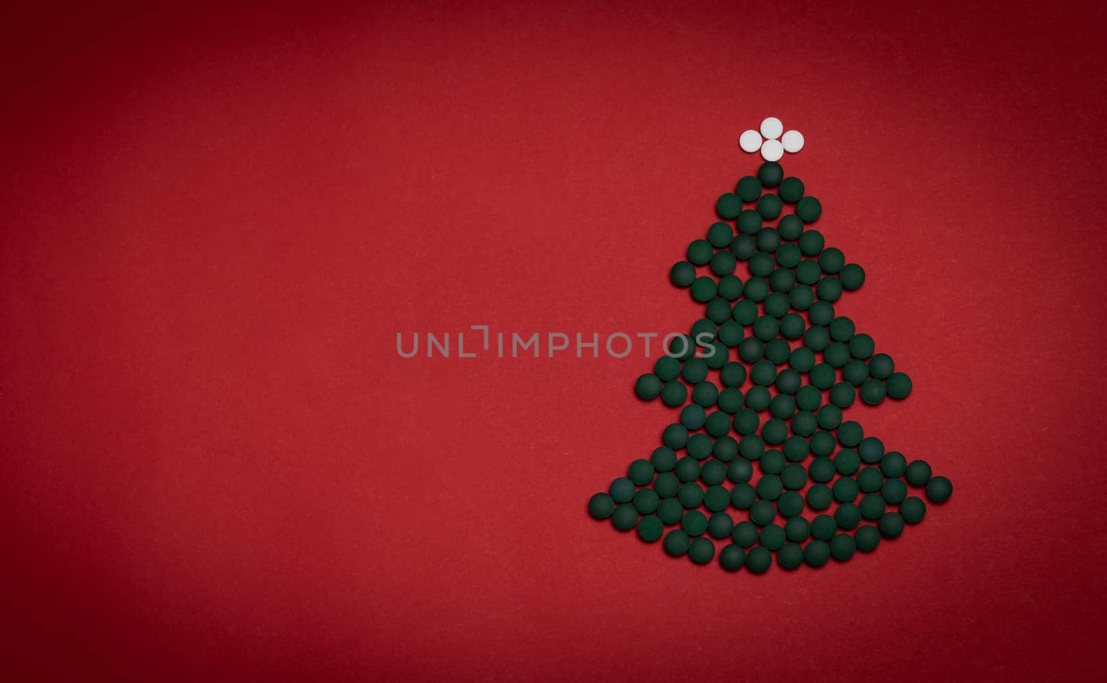 Red background, medicine mockup, Christmas tree made of green white pills,tablets,vitamins spirulina. Merry Christmas, Happy New Year concept, pharmacy postcard,flatly, top view, copy space Horizontal