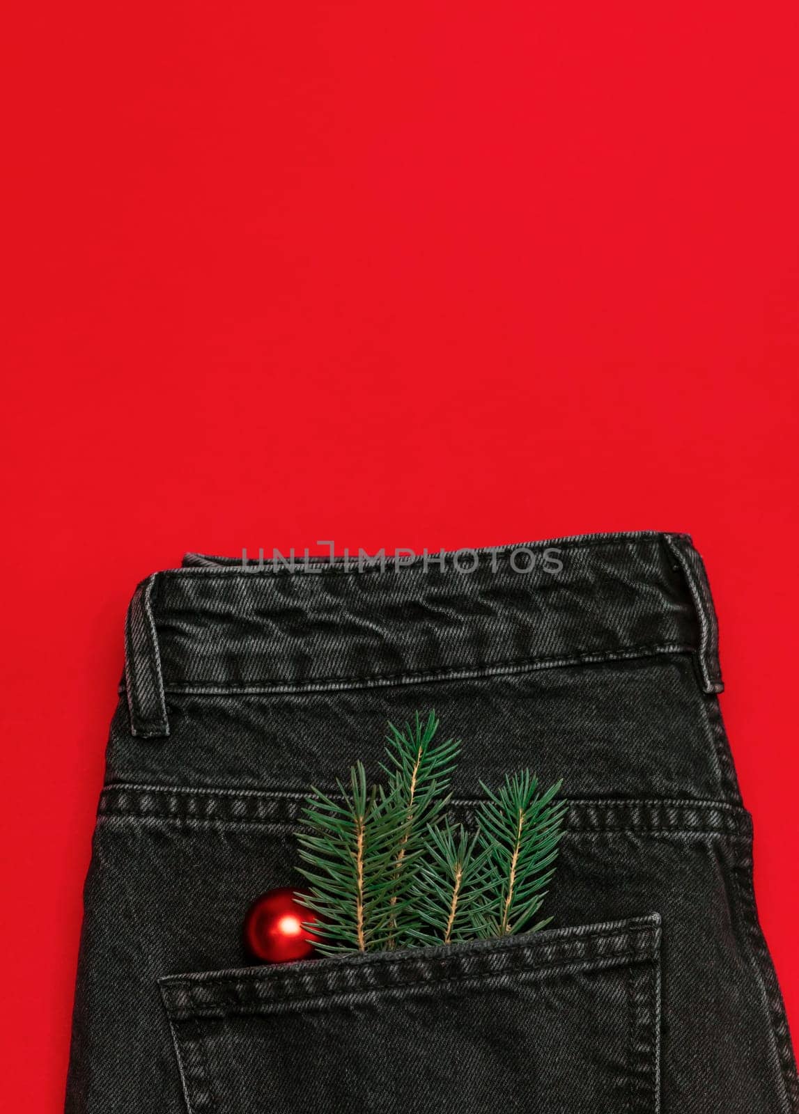 Christmas, New year jeans,denim trousers on red background for store, online shopping ,gray pants with Christmas toy ball and fir limb in pocket. Winter holiday celebration concept. Vertical Flatly