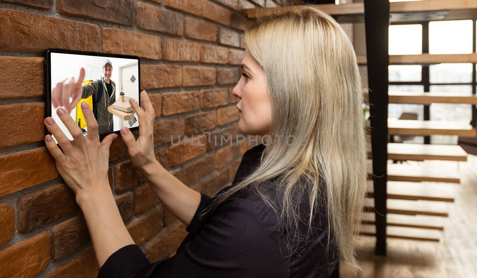 Woman watching delivery man on security camera cctv video on tablet by Andelov13