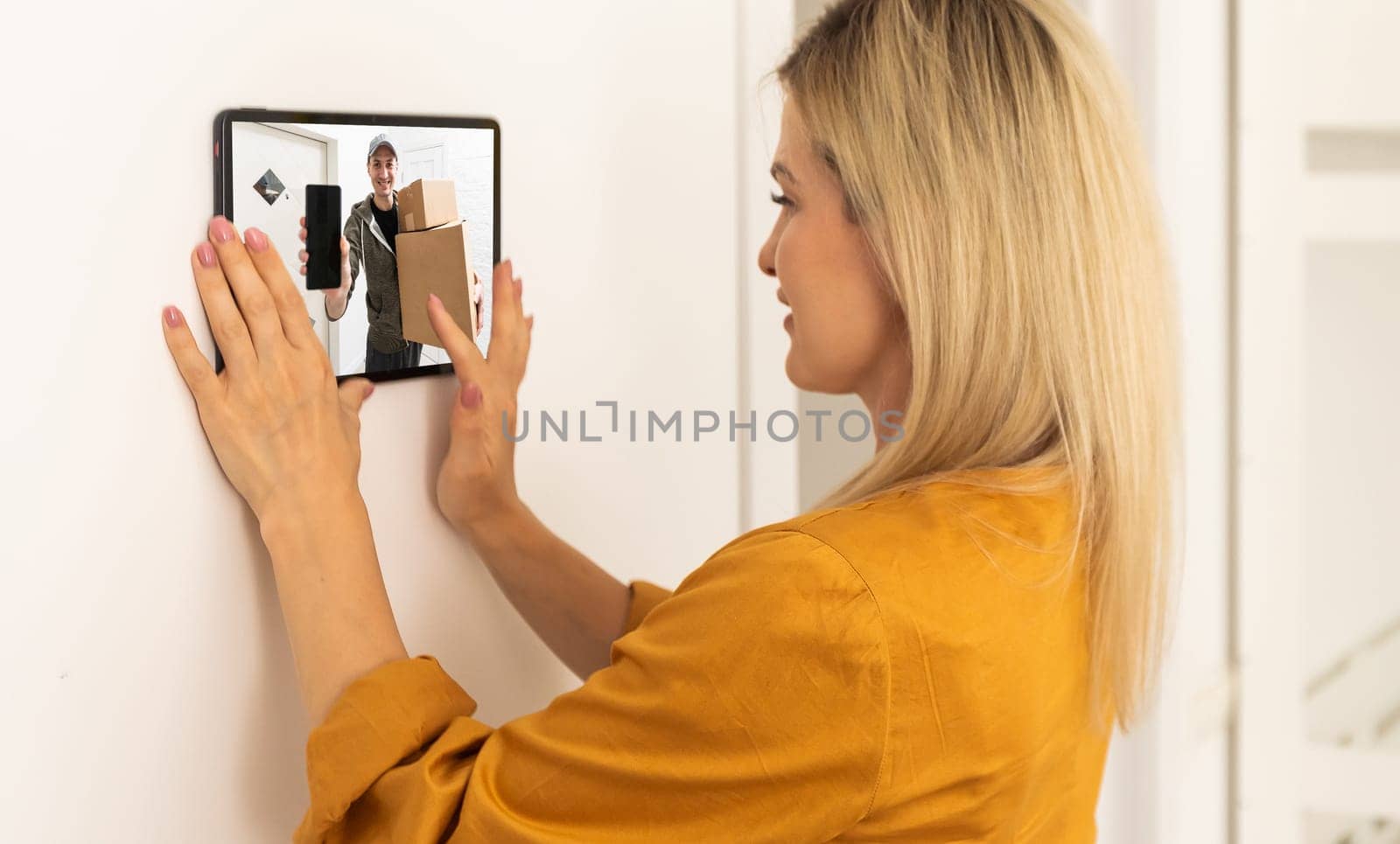 Woman watching delivery man on security camera cctv video on tablet by Andelov13