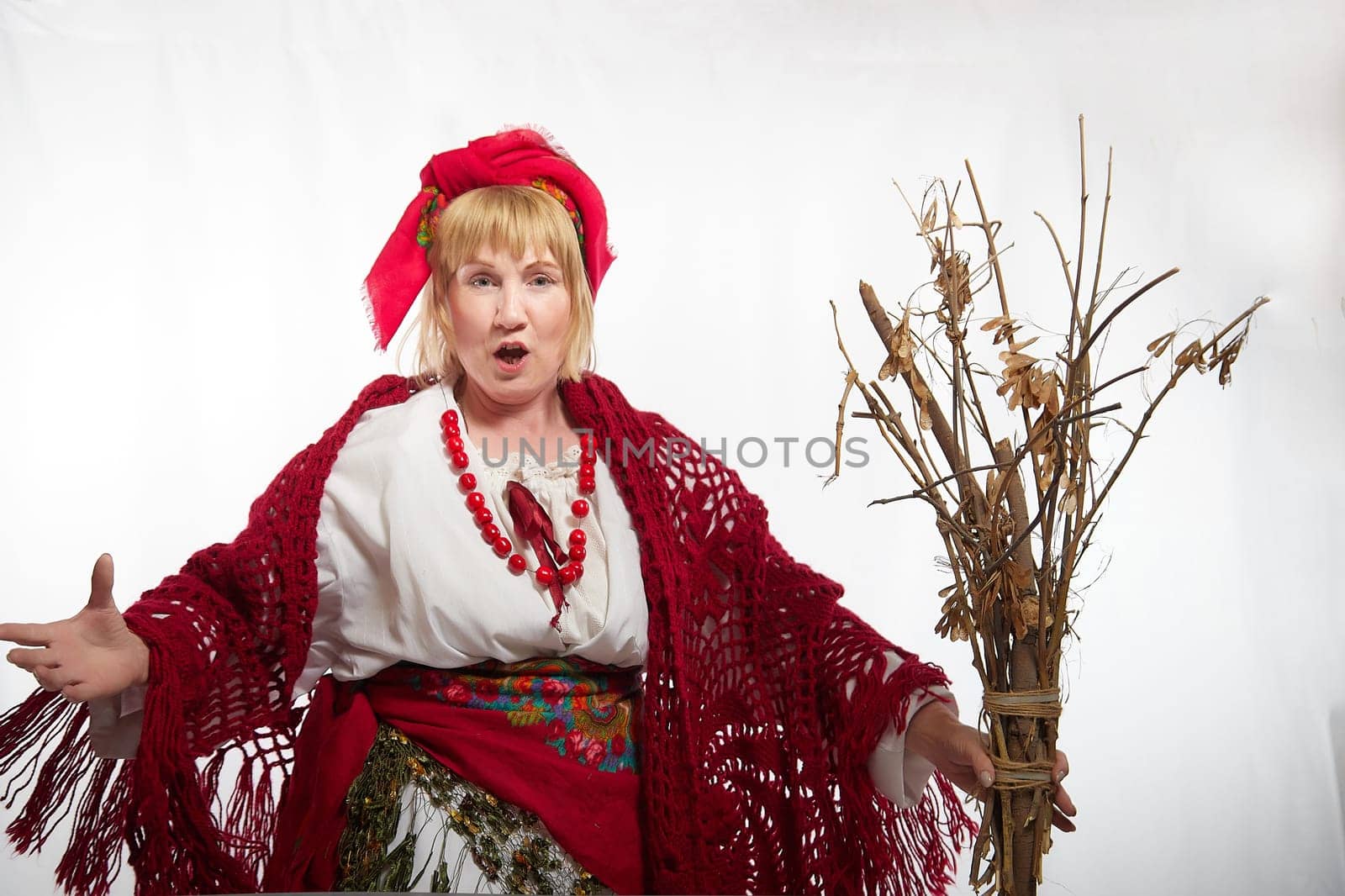 Cheerful funny adult mature woman solokha with broom. Female model baba yaga in clothes of national ethnic Slavic style. Stylized Ukrainian, Belarusian or Russian woman poses in comic photo shoot