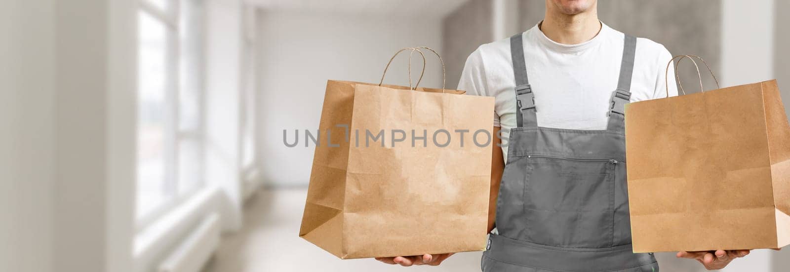 Young handsome delivery man holding paper bag with takeaway food happy with big smile