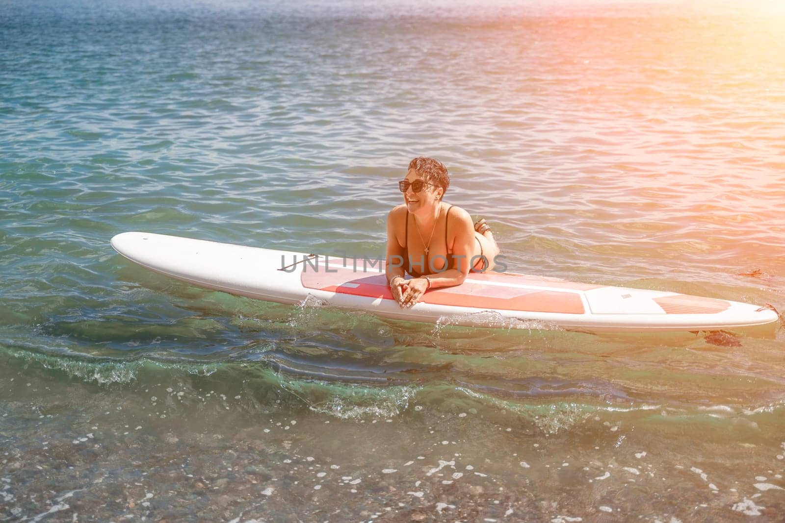 Woman sup sea travel. Sports girl on a surfboard in the sea on a sunny summer day. In a black bathing suit, he sits on a sapa in the sea. Rest on the sea