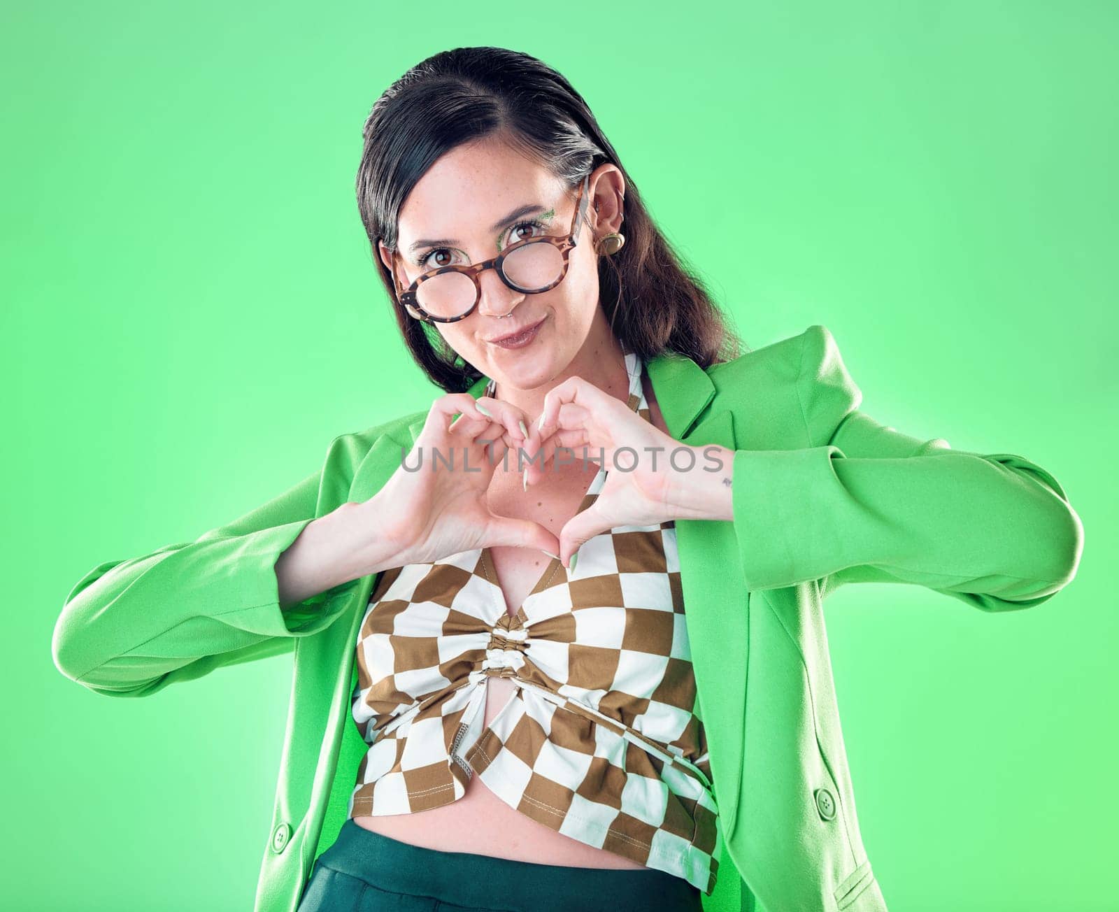 Portrait, hands and heart with a woman on a green background in studio for love, romance or health. Social media, emoji and affection with a trendy person posing or making a hand sign for style.