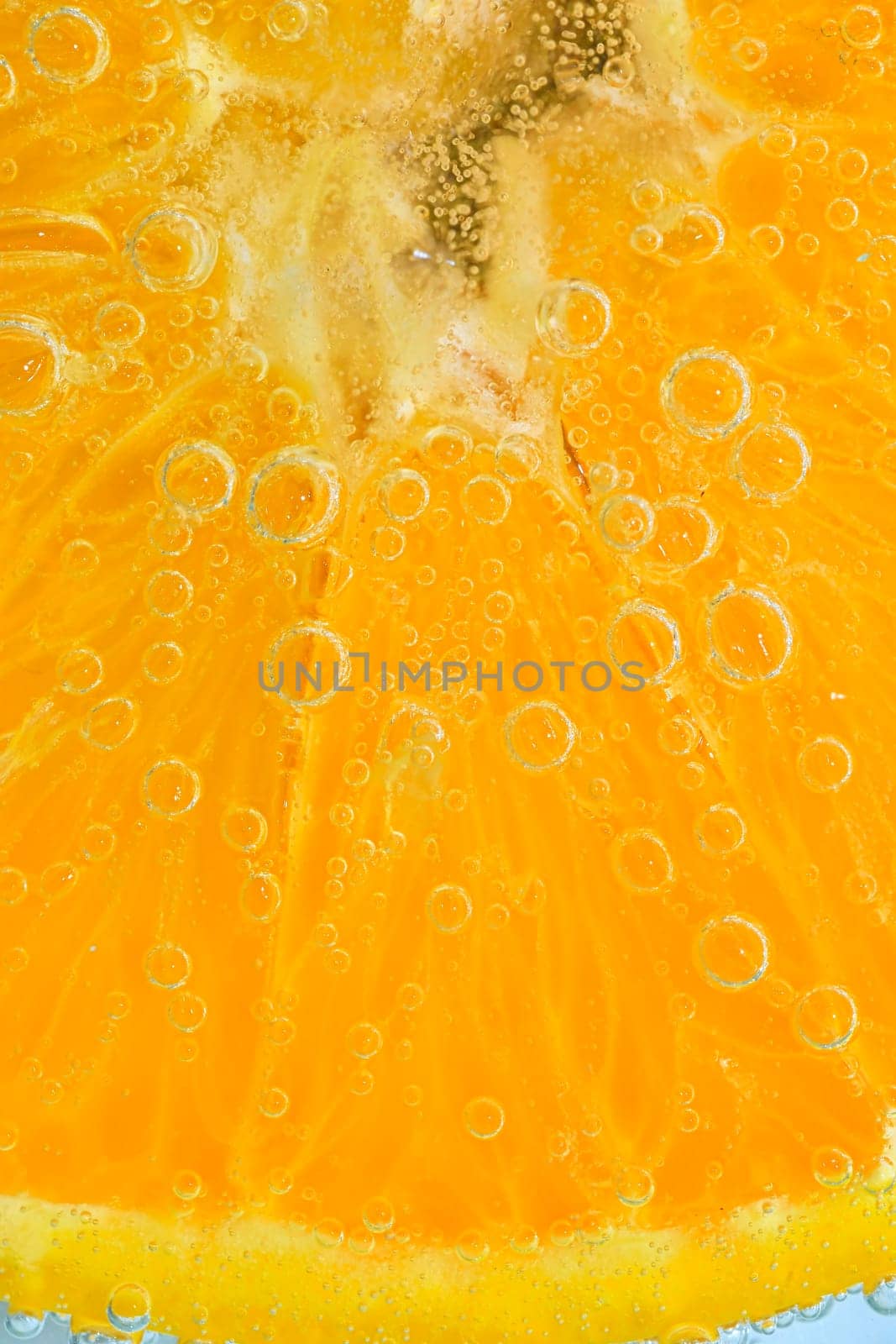 Close-up of juicy orange fruit slice. Slice of ripe orange fruit in sparkling water, close-up. Vertical macro image
