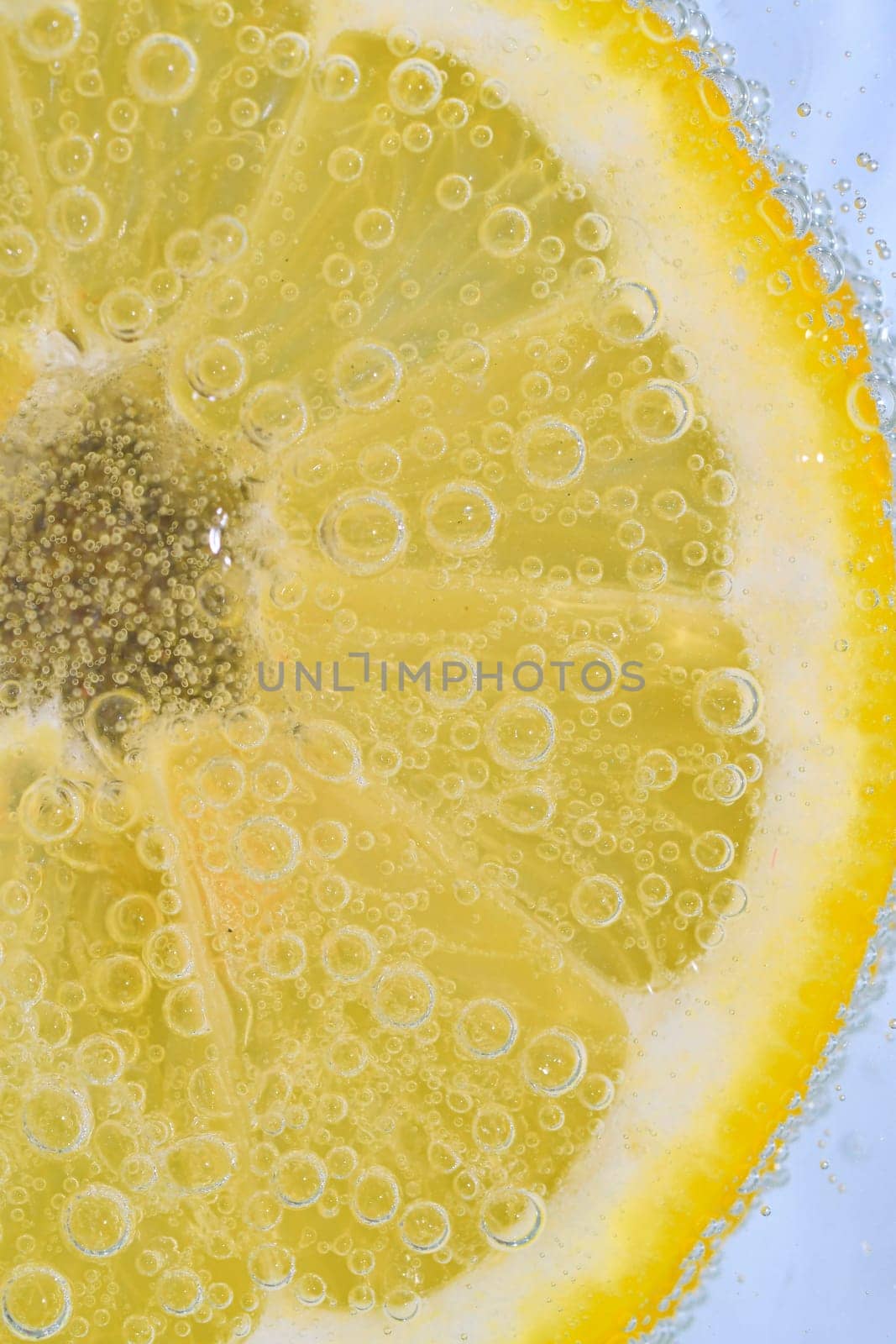 Slice of ripe lemon in water on white background. Close-up of lemon in liquid with bubbles. Slice of ripe citron in sparkling water. Macro image of fruit in carbonated water. by roman_nerud