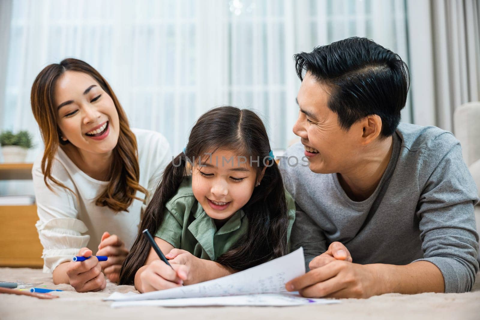 Father, mother and daughter smile drawing art picture together on paper at home, excited Asian family fun lying on floor painting with little child daughter in living room, Happy family activity enjoy