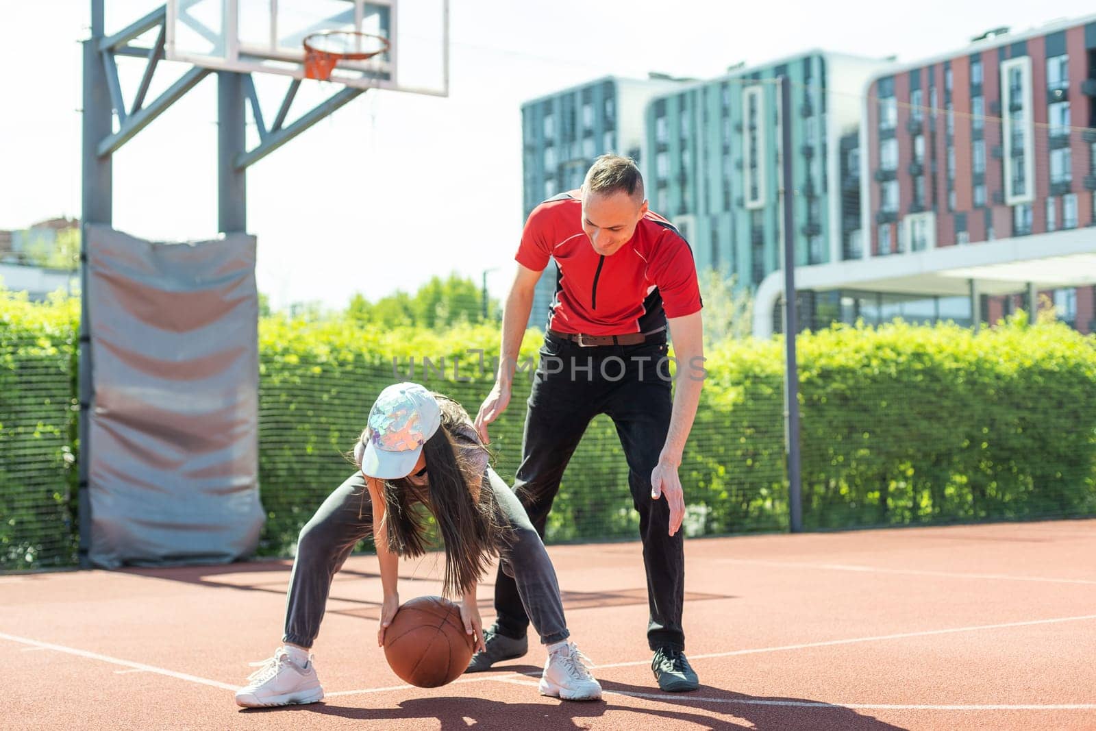 Happy father and teenage daughter playing basketball outside at court.