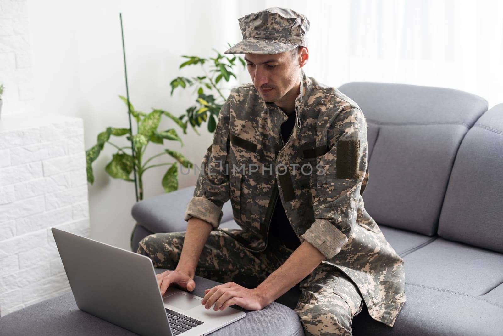 partial view of army soldier using laptop on couch by Andelov13