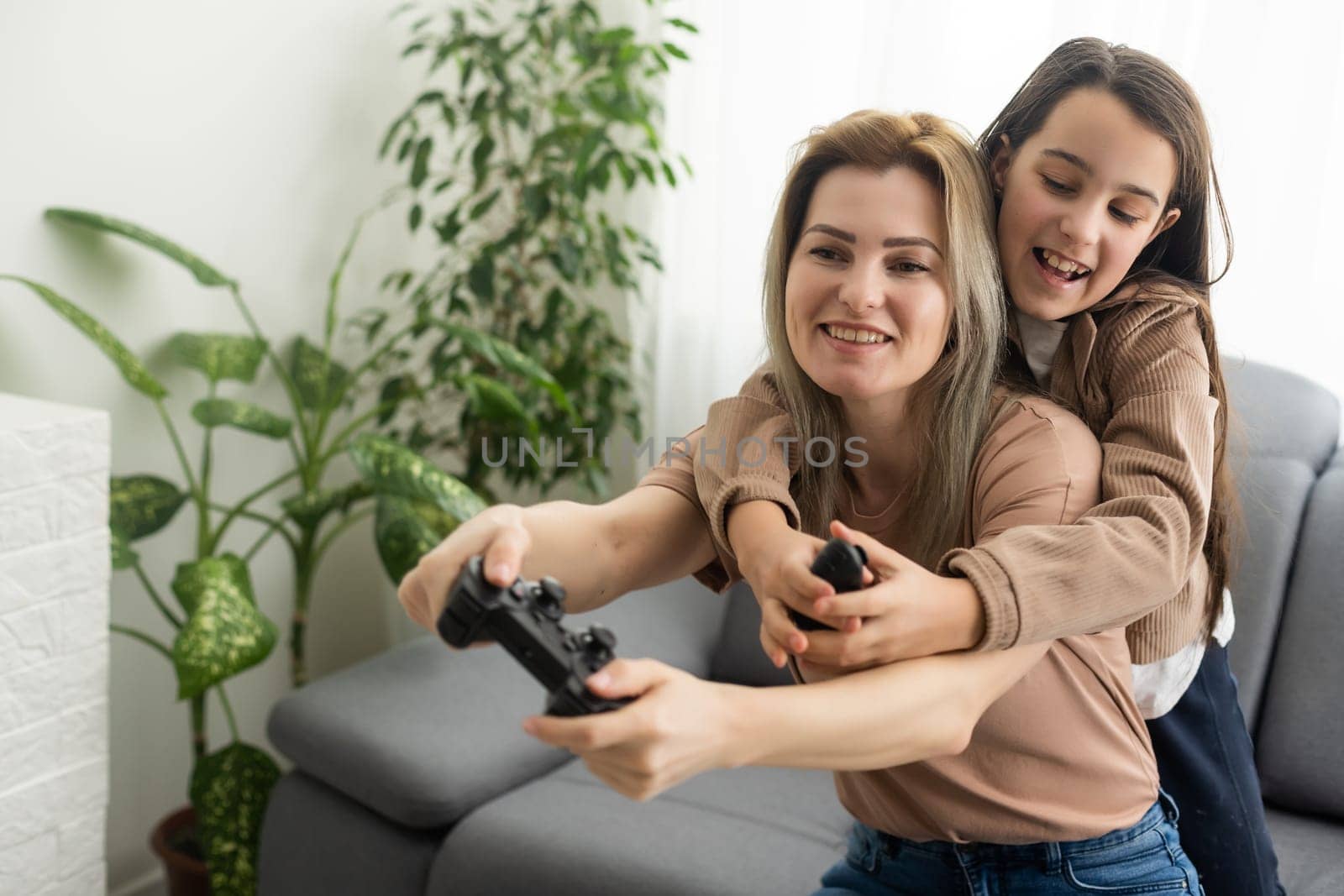 good relationship cute little girl with young mother using joystick playing video game sitting together in living room wooden floor enjoying family holiday.