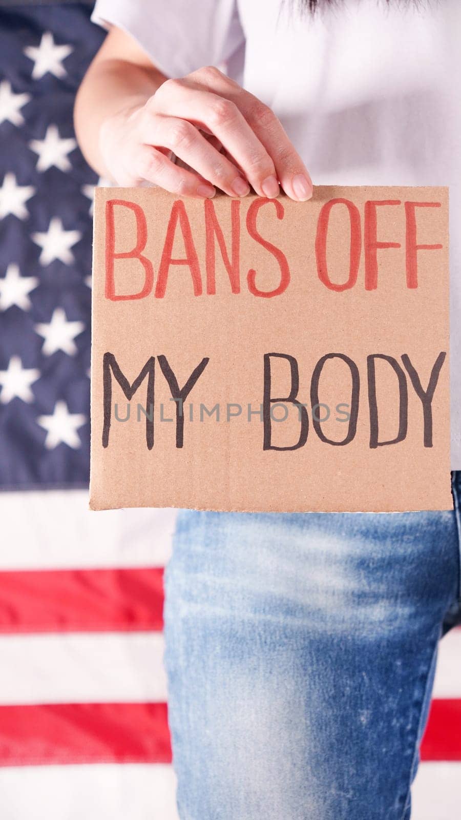 Woman holding a sign Bans Off My Body American flag on background. Protest against anti abortion law. Women's strike. Womens rights freedom