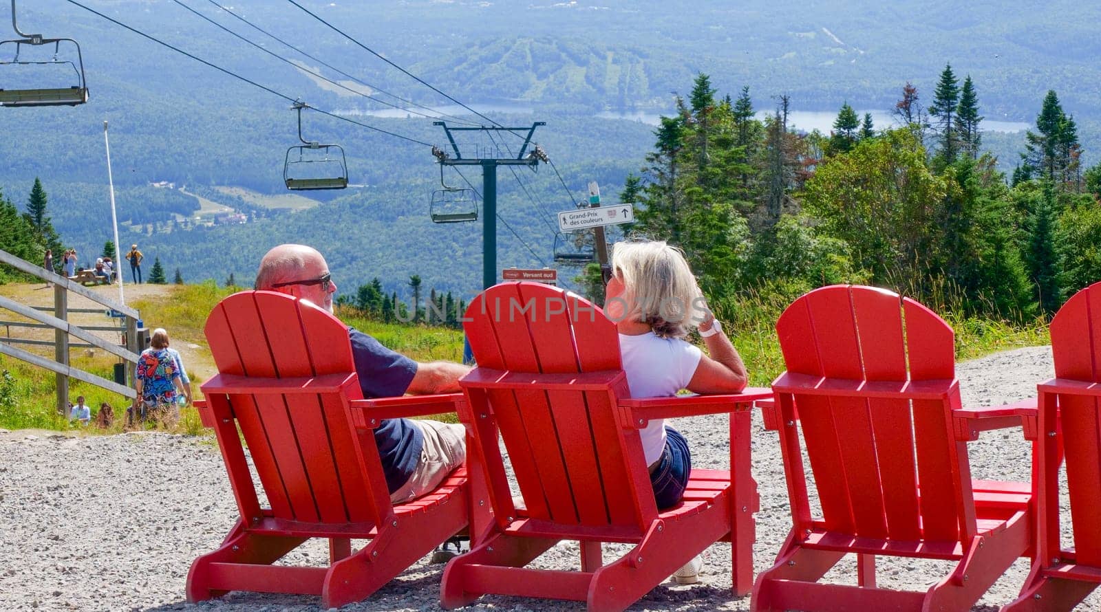 Sightseeing mountain views at Mont Tremblant ski Resort in summer. Tourists enjoying sitting at red chairs at ski resort village. Mont-Tremblant, Quebec, Canada - 22.09.2022 by JuliaDorian