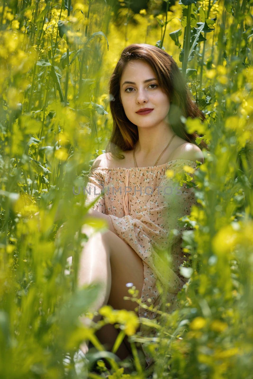 Young woman surrounded by canola flowers. Spring blossom field.