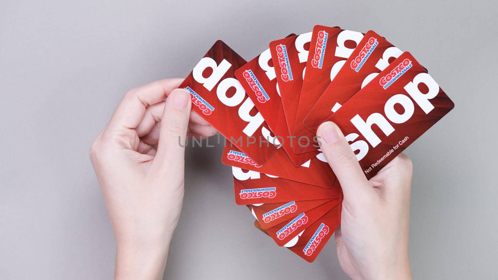 Hand holding pile of Costco wholesale red color gift cards on grey background. Shopping, gift card, shop. Gatineau QC Canada - December 21, 2022. by JuliaDorian