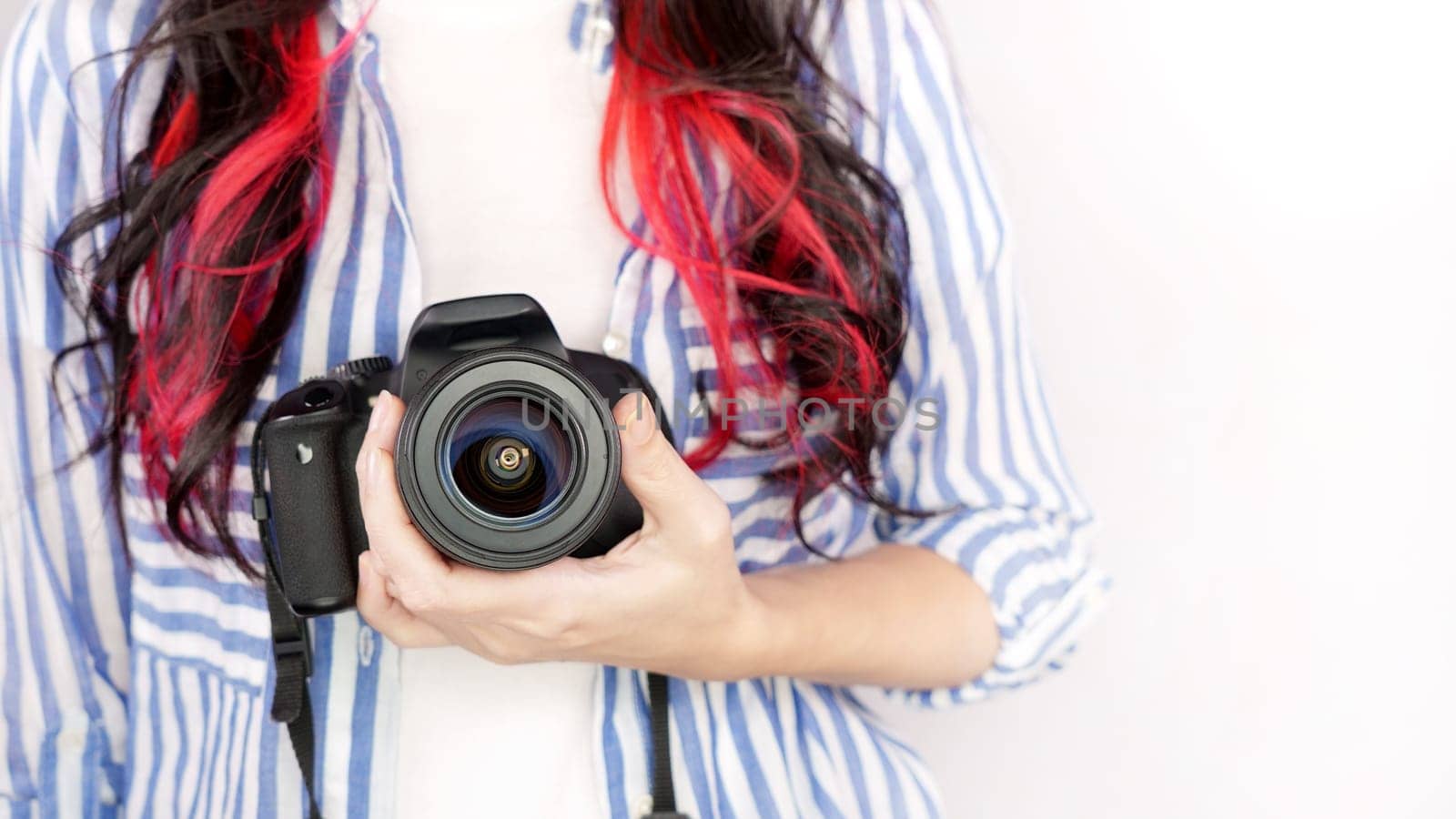 Photographer holding dslr camera. Self portrait, front view. Faceless nice woman with brown red hair in a tshirt with hands holding photo camera white background