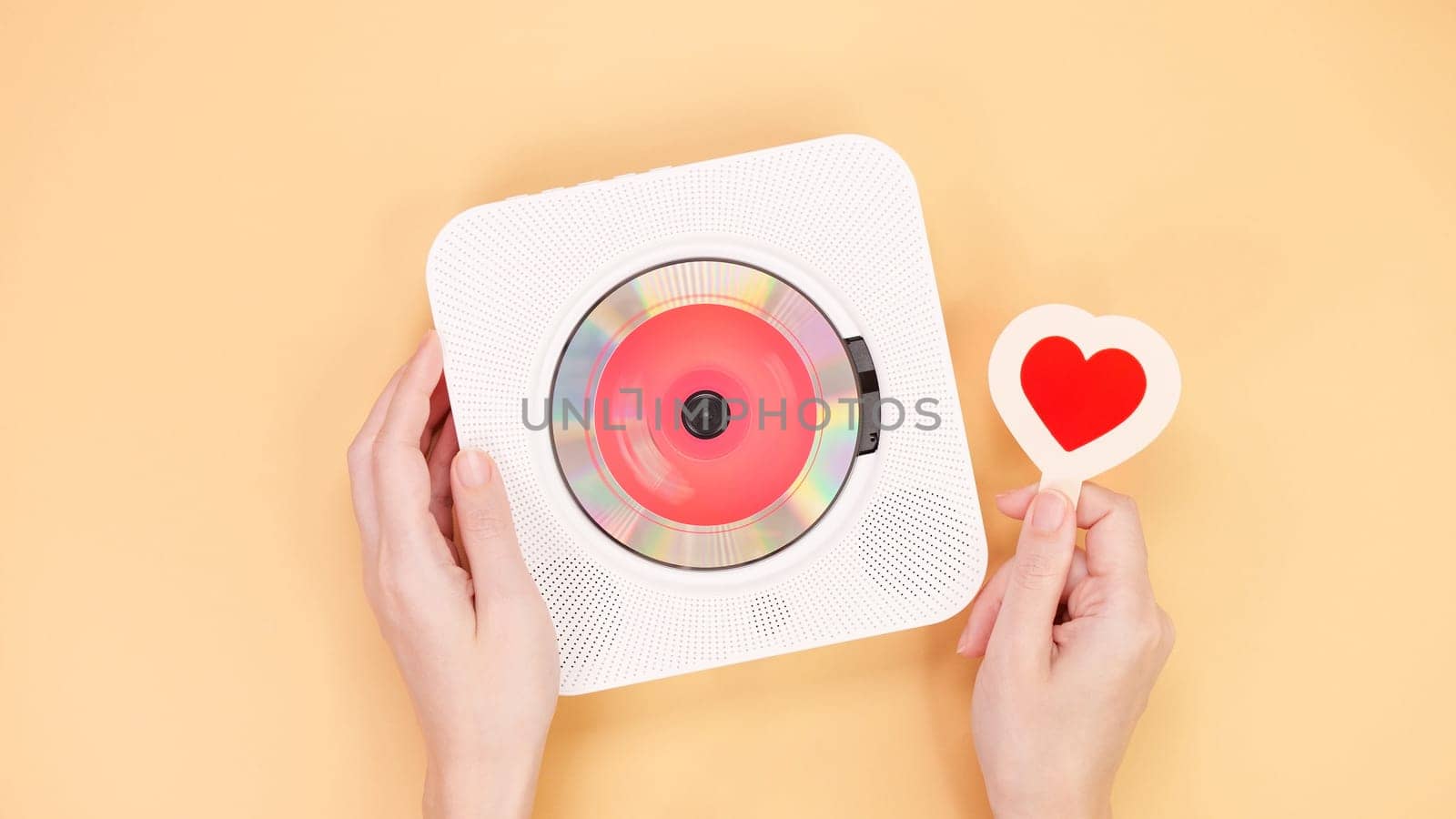 Hands holding white cd player with red disc and heart shape gift card on yellow background. Love music, Valentine day, Greeting, retro Love song, space for text. by JuliaDorian