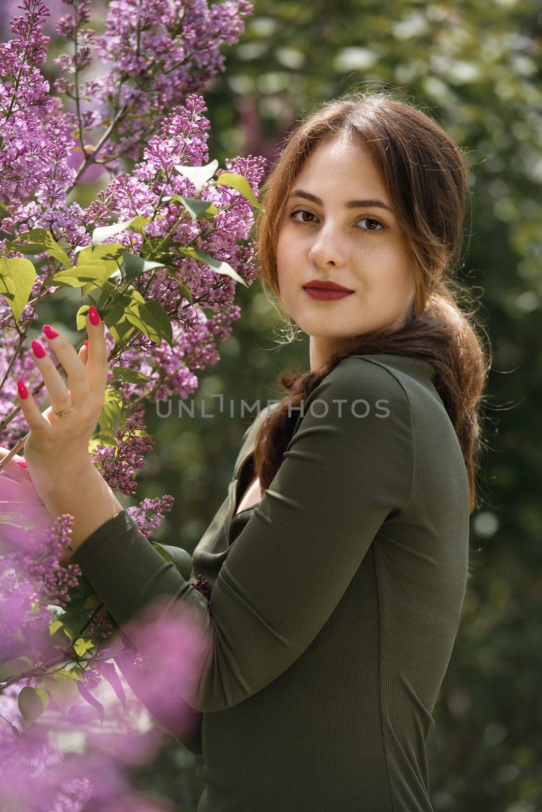 Portrait of a beautiful young woman surrounded by lilac flowers.