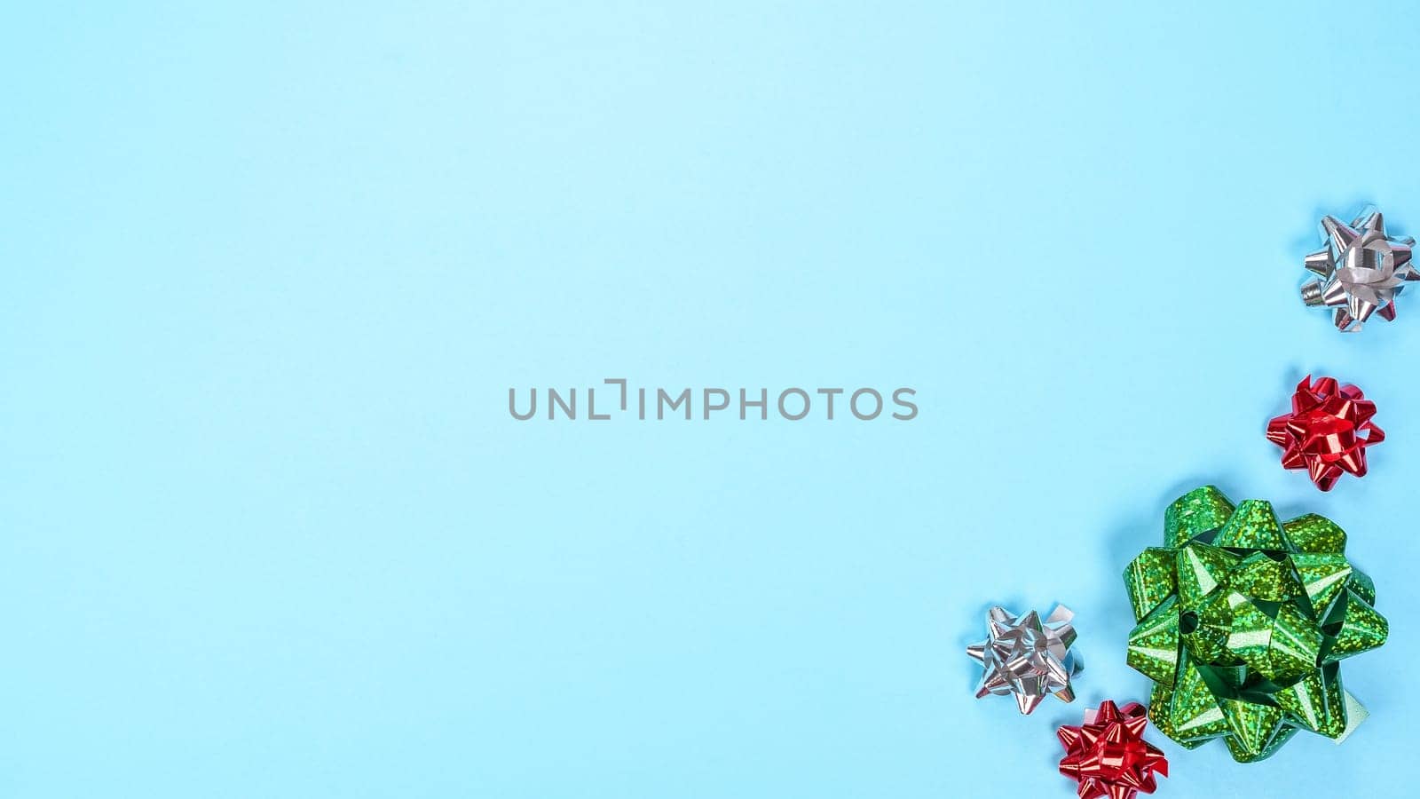 Beautiful Christmas red green silver present ribbon bow over light blue background with space for text. New Year gift. Many colorful bows on blue. Top view New Year Christmas flatlay with decorations.