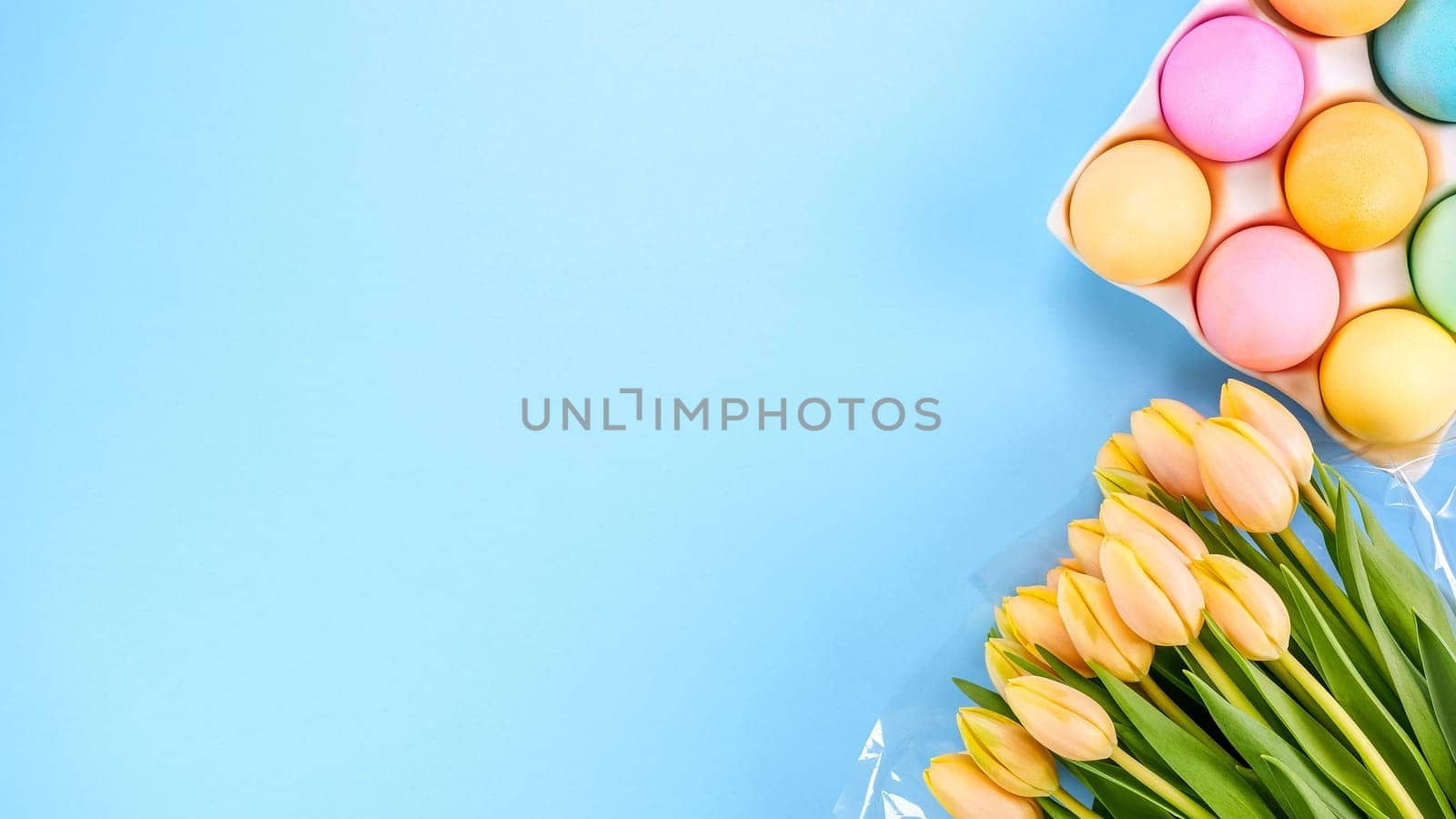 Spring flat lay with fresh yellow tulips colorful eggs on blue background. Easter, Mother day, birthday or Anniversary with copy-space. Sweet rainbow color Easter eggs, small pastel colors