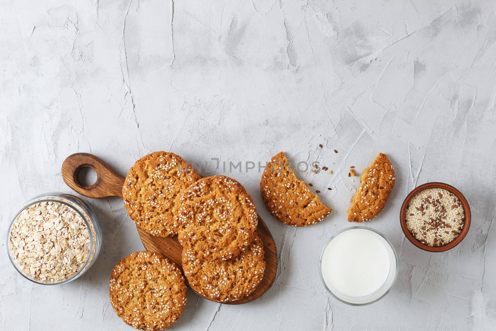 Oatmeal cookies with sesame seeds and flax seeds on a gray background with a jar of oatmeal and a glass of milk.Copy space by lara29