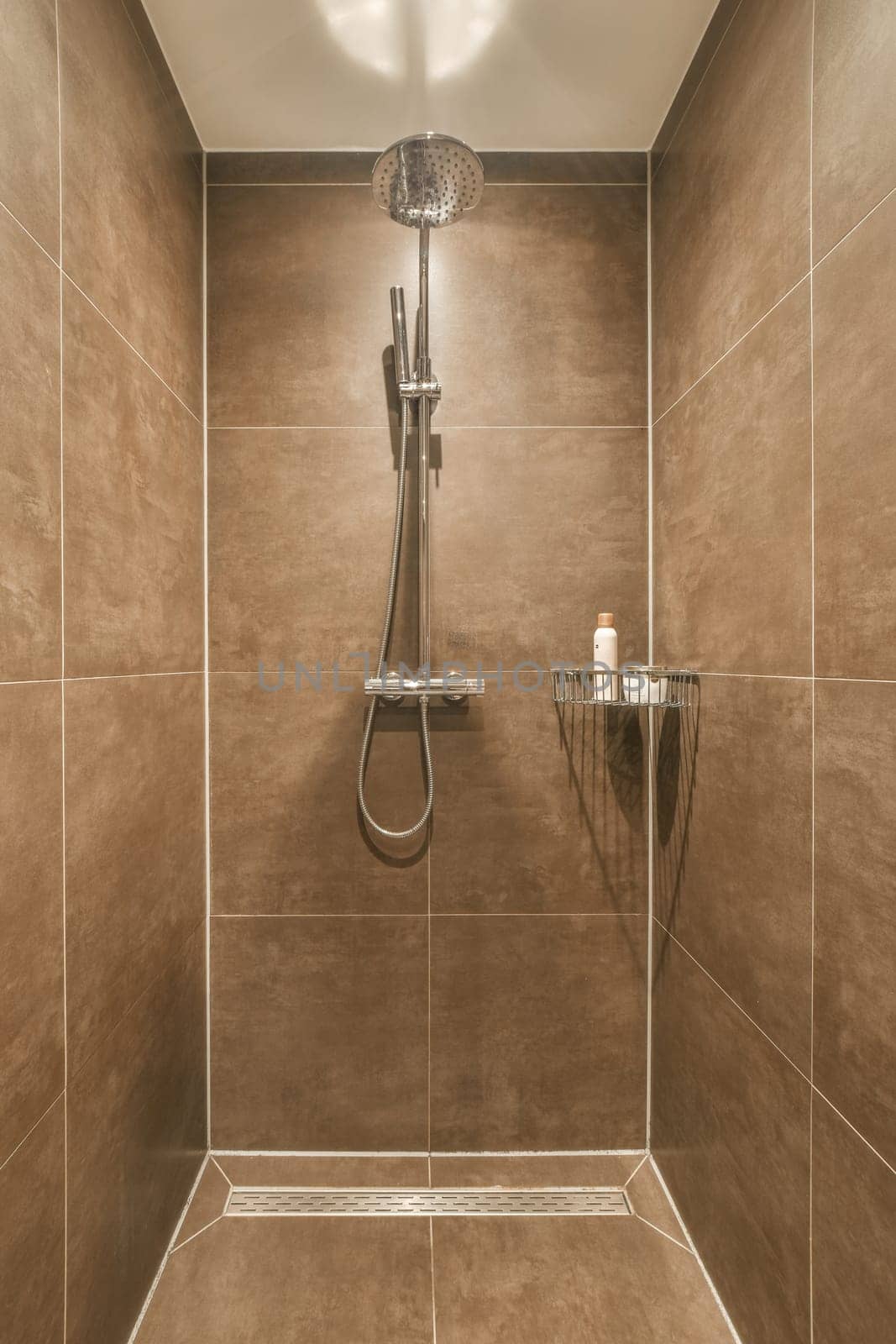 a shower room with brown tiles on the walls and tile around the tub, hand held by an adjustable shower head
