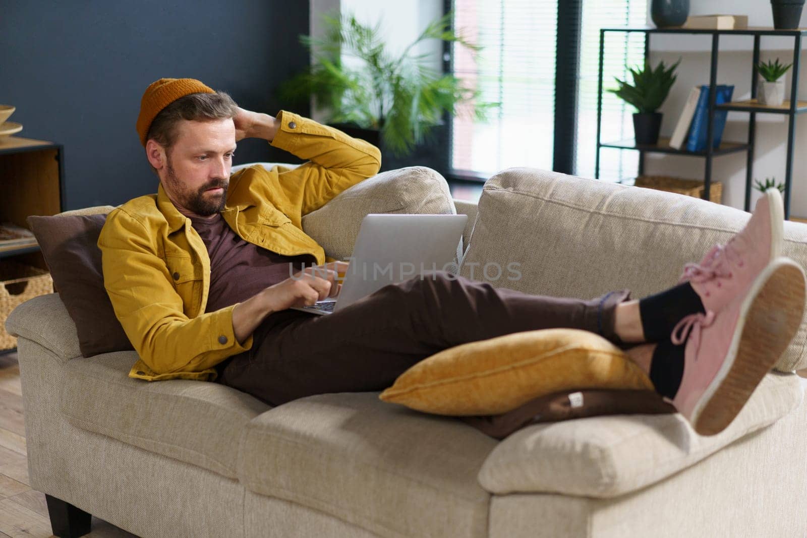 Wise programmer deep in thought, contemplating how to write code for program. Freelancer comfortably laying on sofa while working from home, embracing flexibility and benefits of remote work. . High quality photo