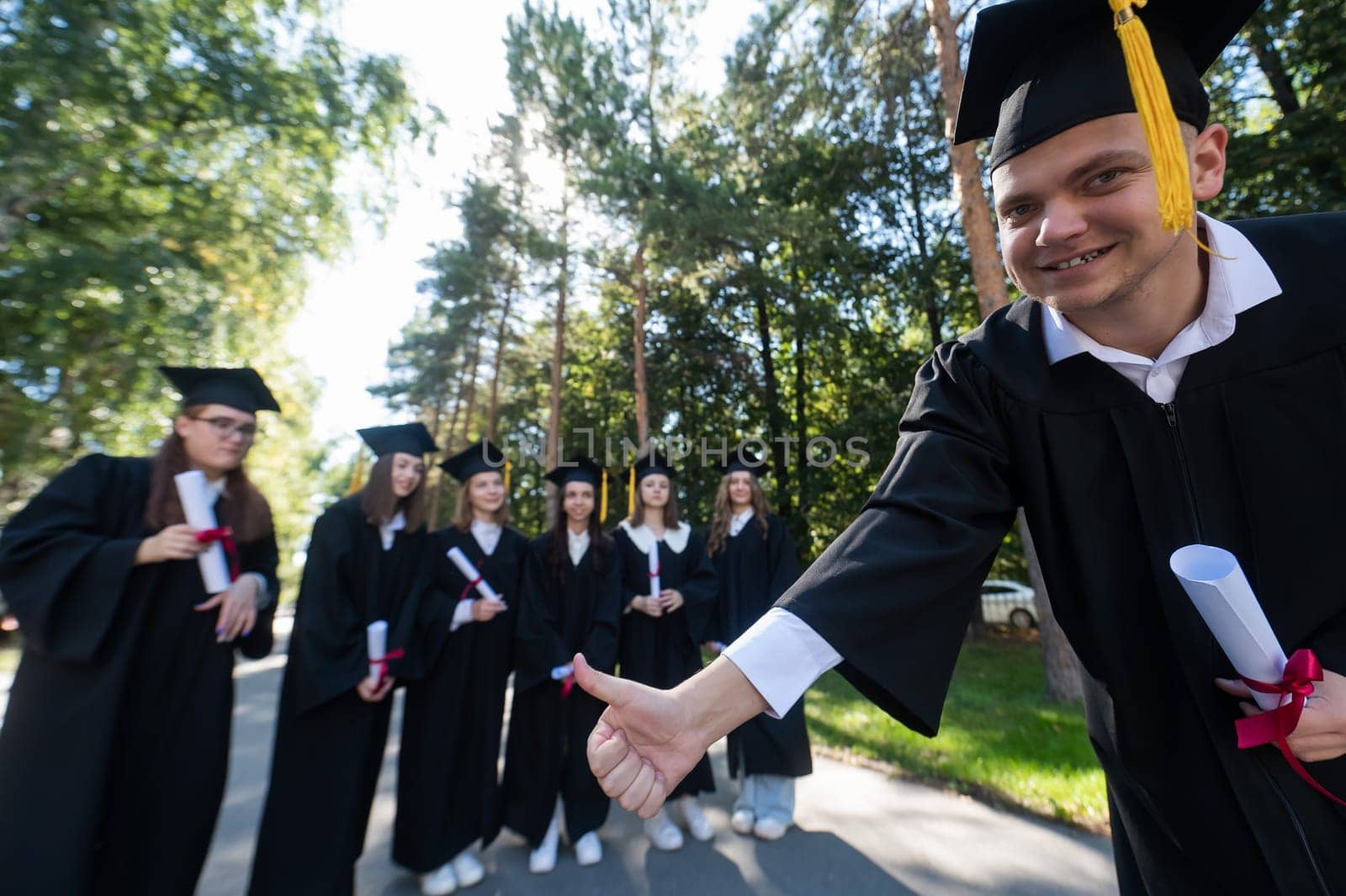 Happy young caucasian male graduate showing thumbs up. A group of graduate students outdoors