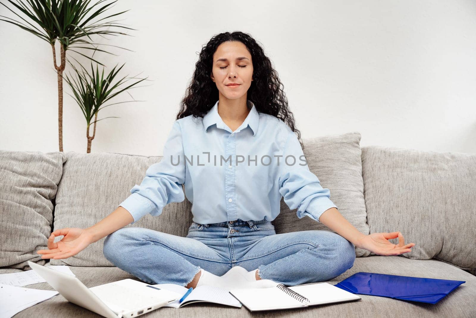 Beautiful young woman mixed race close your eyes and rest during work break. Nice relaxation sitting on sofa in yoga pose