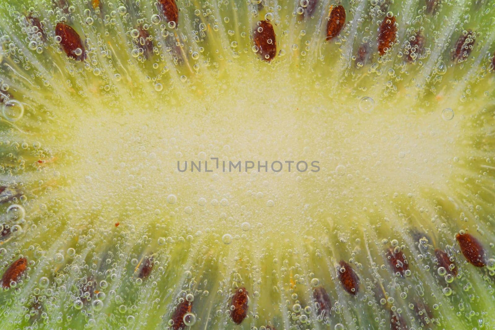 Close-up of a kiwi fruit slice in liquid with bubbles. Slice of ripe kiwi fruit in water. Close-up of fresh kiwi slice covered by bubbles. Macro horizontal image. by roman_nerud