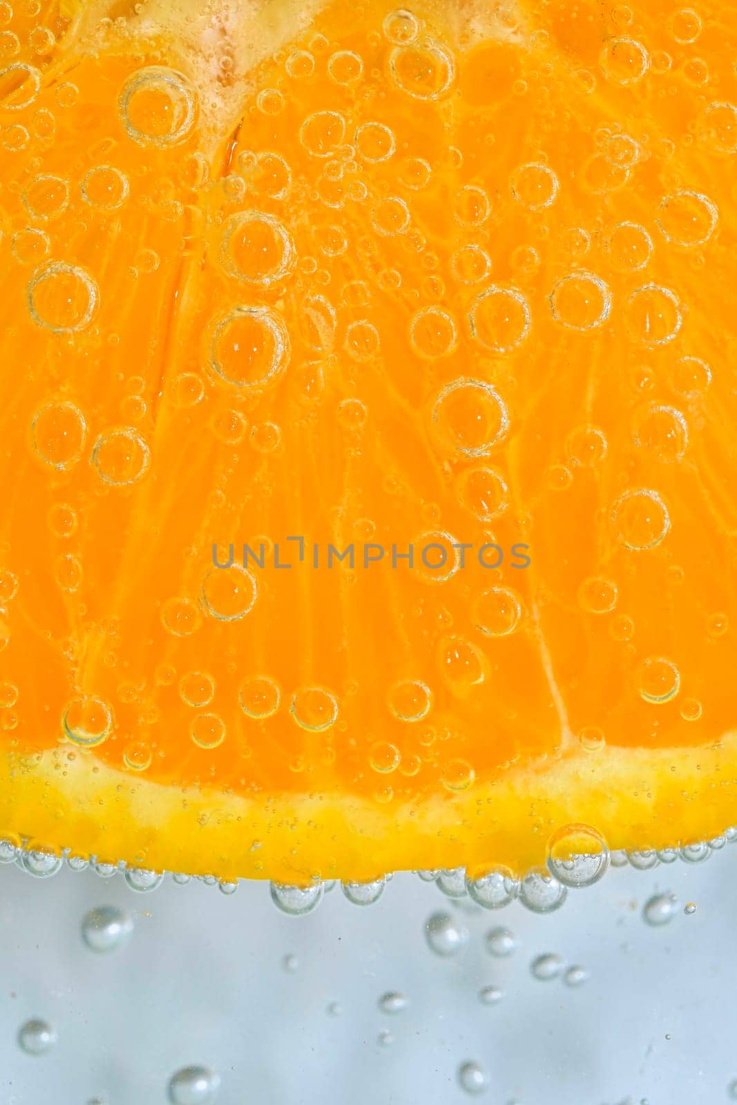 Slice of ripe orange fruit in water on white background. Close-up of orange fruit in liquid with bubbles. Slice of ripe orange fruit in sparkling water. Macro image of fruit in carbonated water