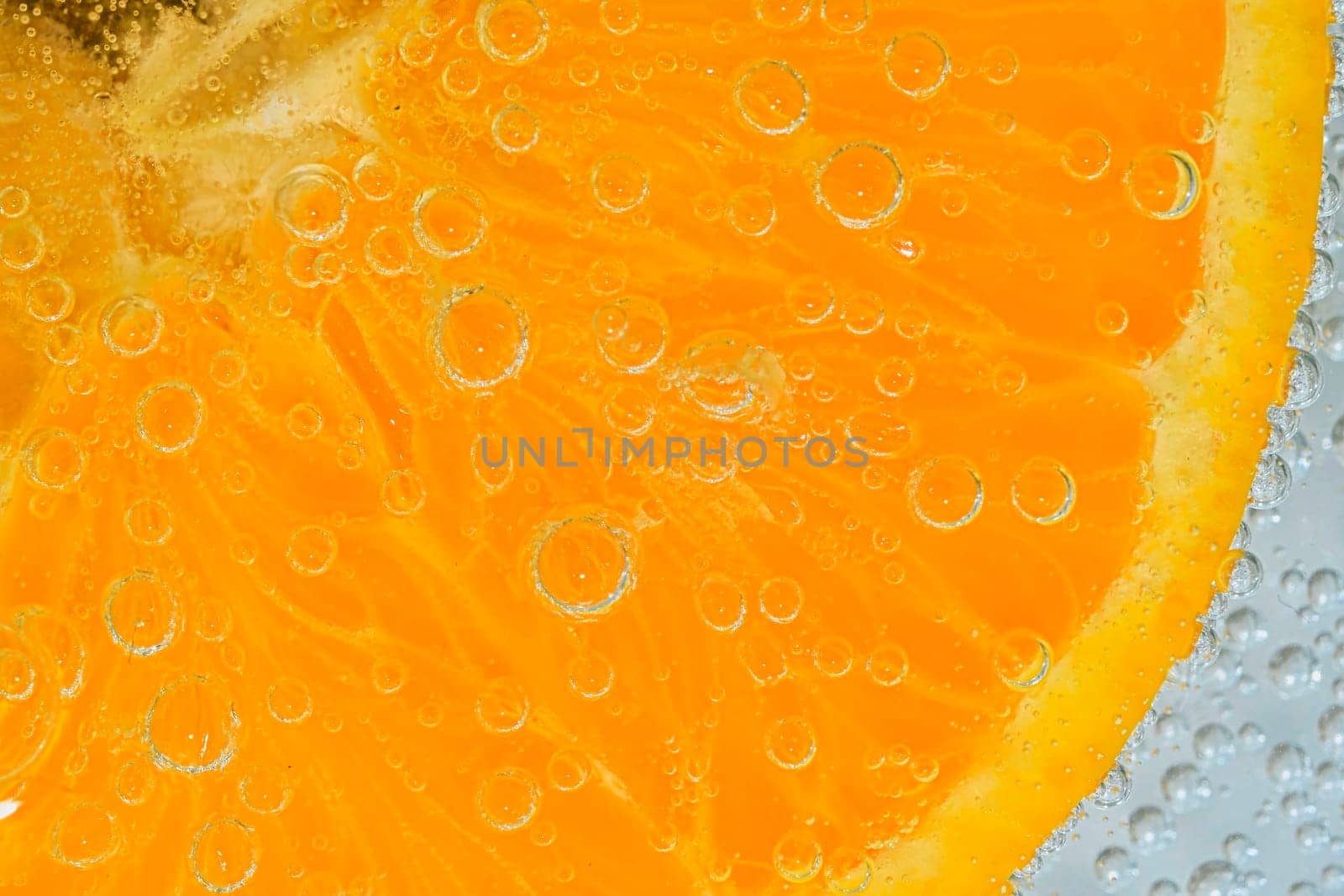Close-up of an orange fruit slice in liquid with bubbles. Slice of ripe orange fruit in water. Close-up of fresh orange fruit slice covered by bubbles. Macro horizontal image. by roman_nerud