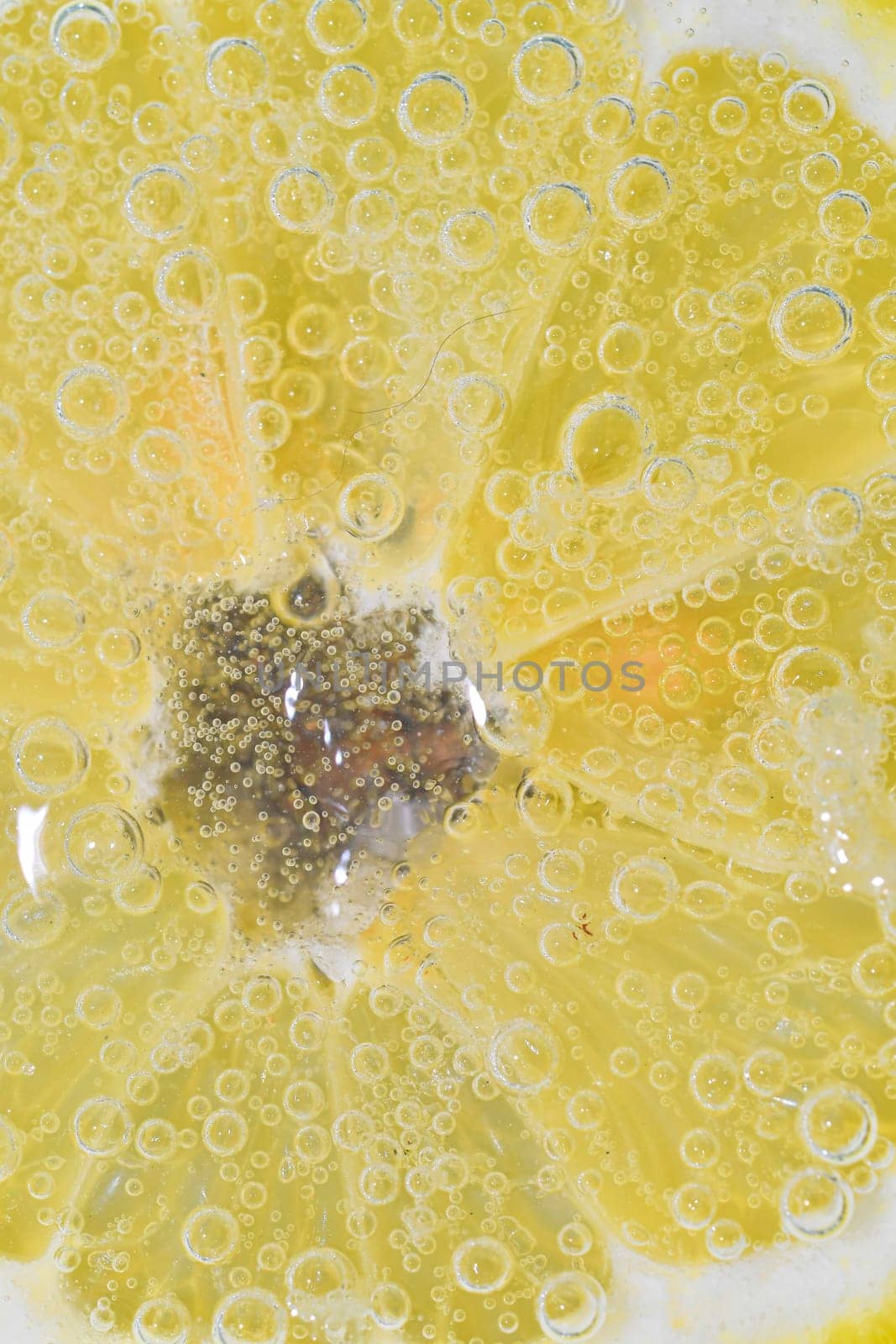 Slice of ripe lemon in water. Close-up of lemon in liquid with bubbles. Slice of ripe citron in sparkling water. Macro image of fruit in carbonated water. by roman_nerud