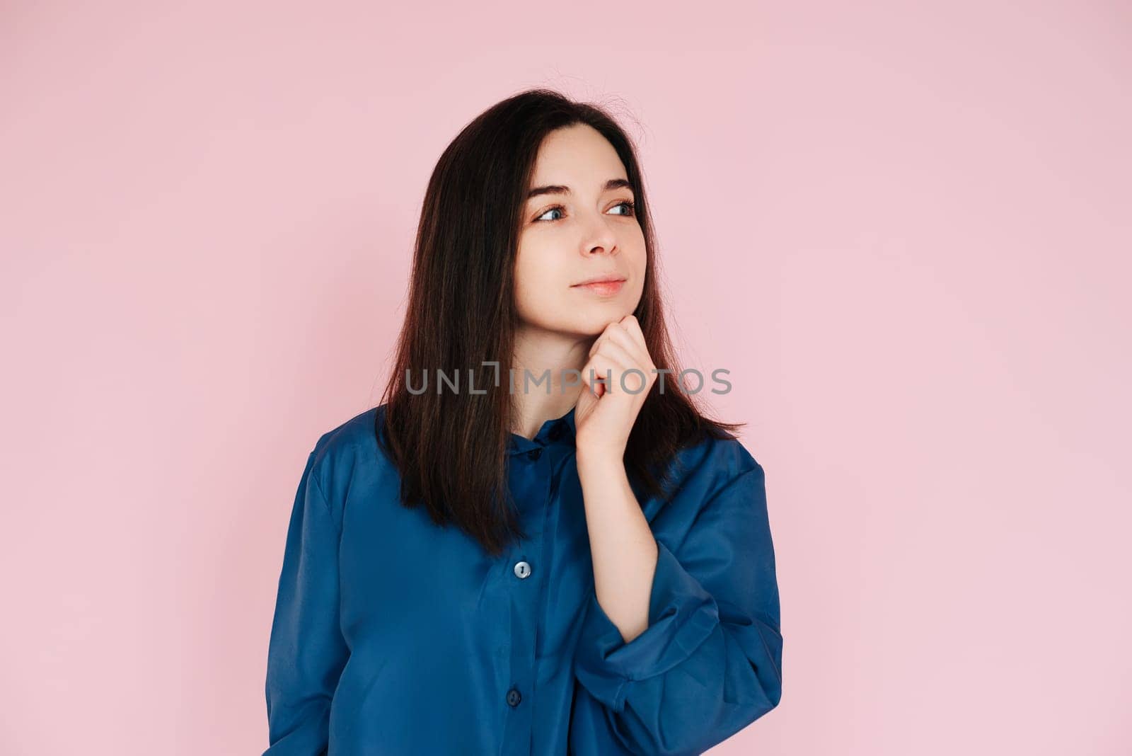 Serenity and Contemplation: Mindful Portrait of a Beautiful Girl with Hand on Chin, Gazing into Empty Space, Isolated on a Calming Pink Background.
