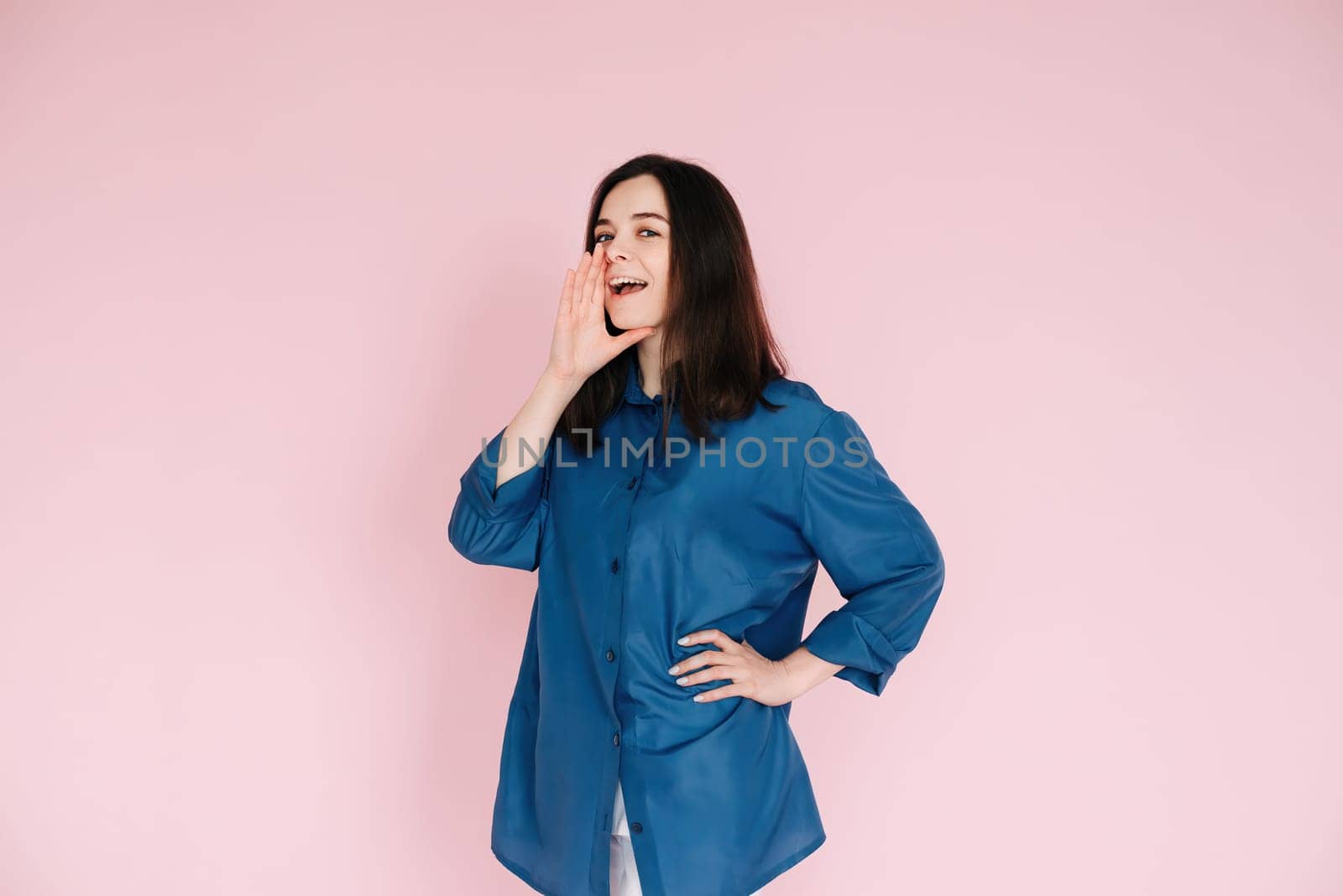 Excited Girl Sharing Breaking News: Hand Near Open Mouth Conveying Surprise and Delivering Important Information in an Empty Space, Isolated on a Pink Background.