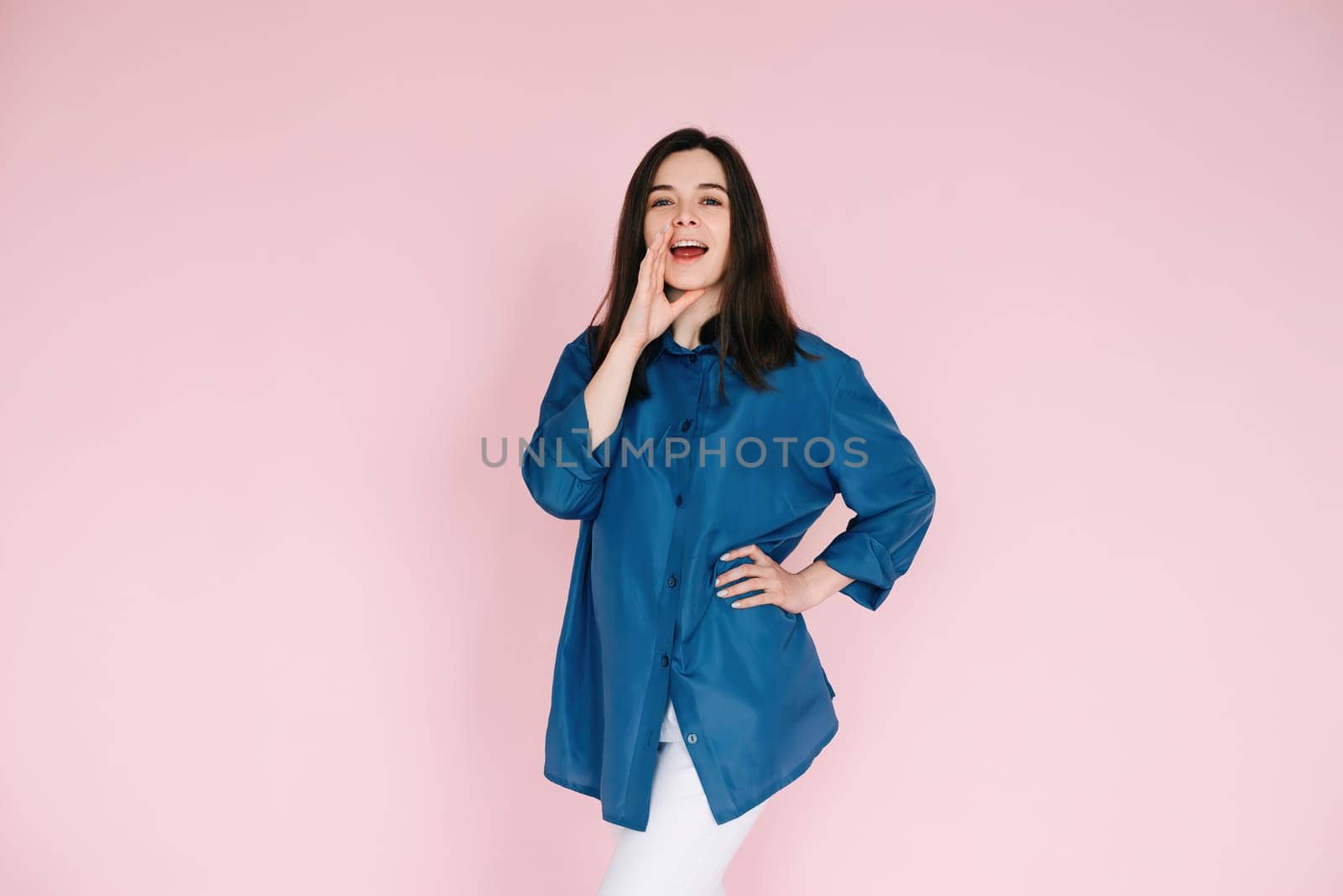 Excited Girl Sharing Breaking News: Hand Near Open Mouth Conveying Surprise and Delivering Important Information in an Empty Space, Isolated on a Pink Background.