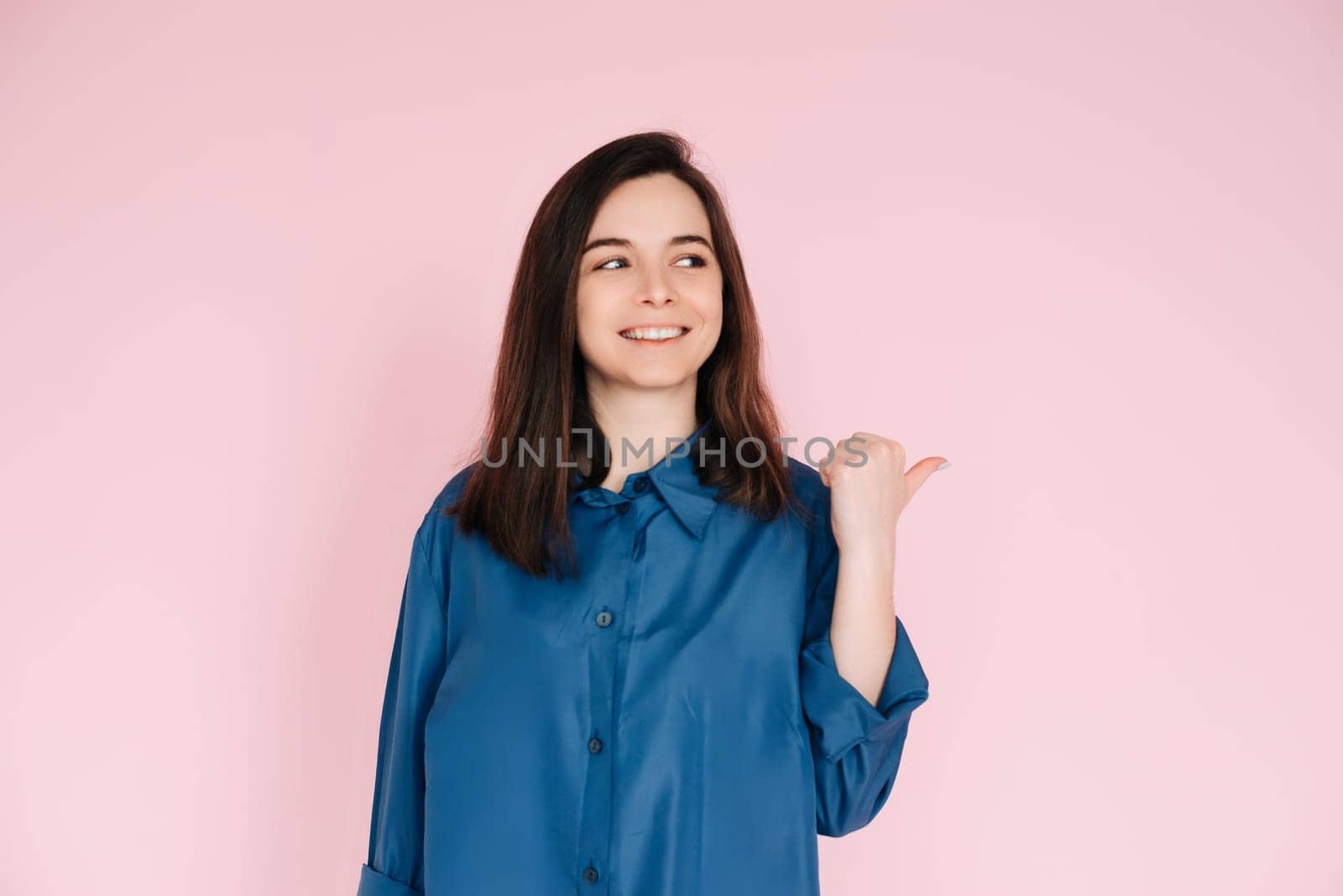 Radiant Portrait of Beautiful Woman with Joyful Smile, Pointing Finger and Looking at Empty Space, Isolated on Pink Background - News and Excitement Concept.